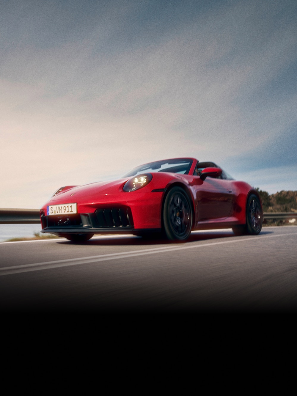 Ein roter Porsche 911 fährt auf einer Straße mit Natur im Hintergrund.