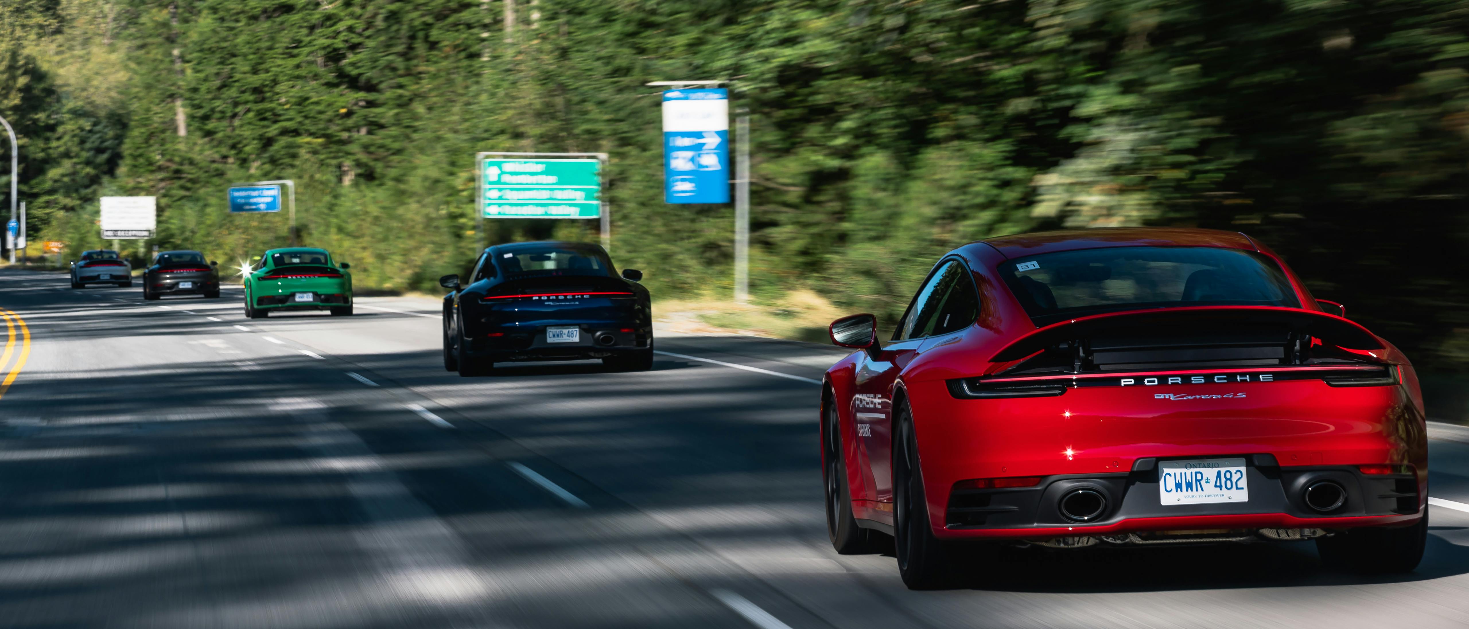 Un groupe de Porsche 911 roulant en file indienne sur une autoroute de campagne.