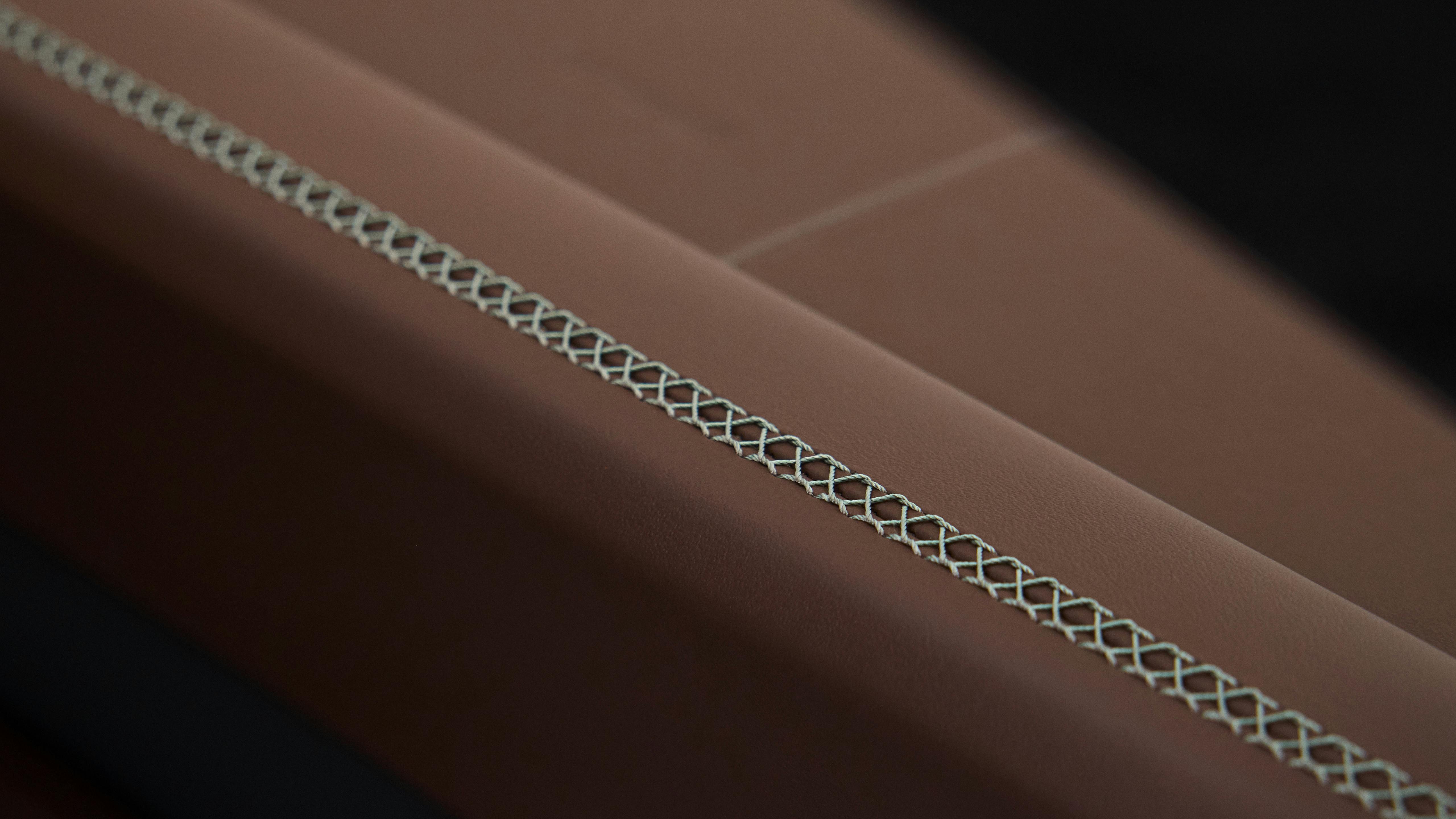 Detail of a brown leather surface in a Porsche 911 Carrera interior with turquoise decorative cross-stitch seam.
