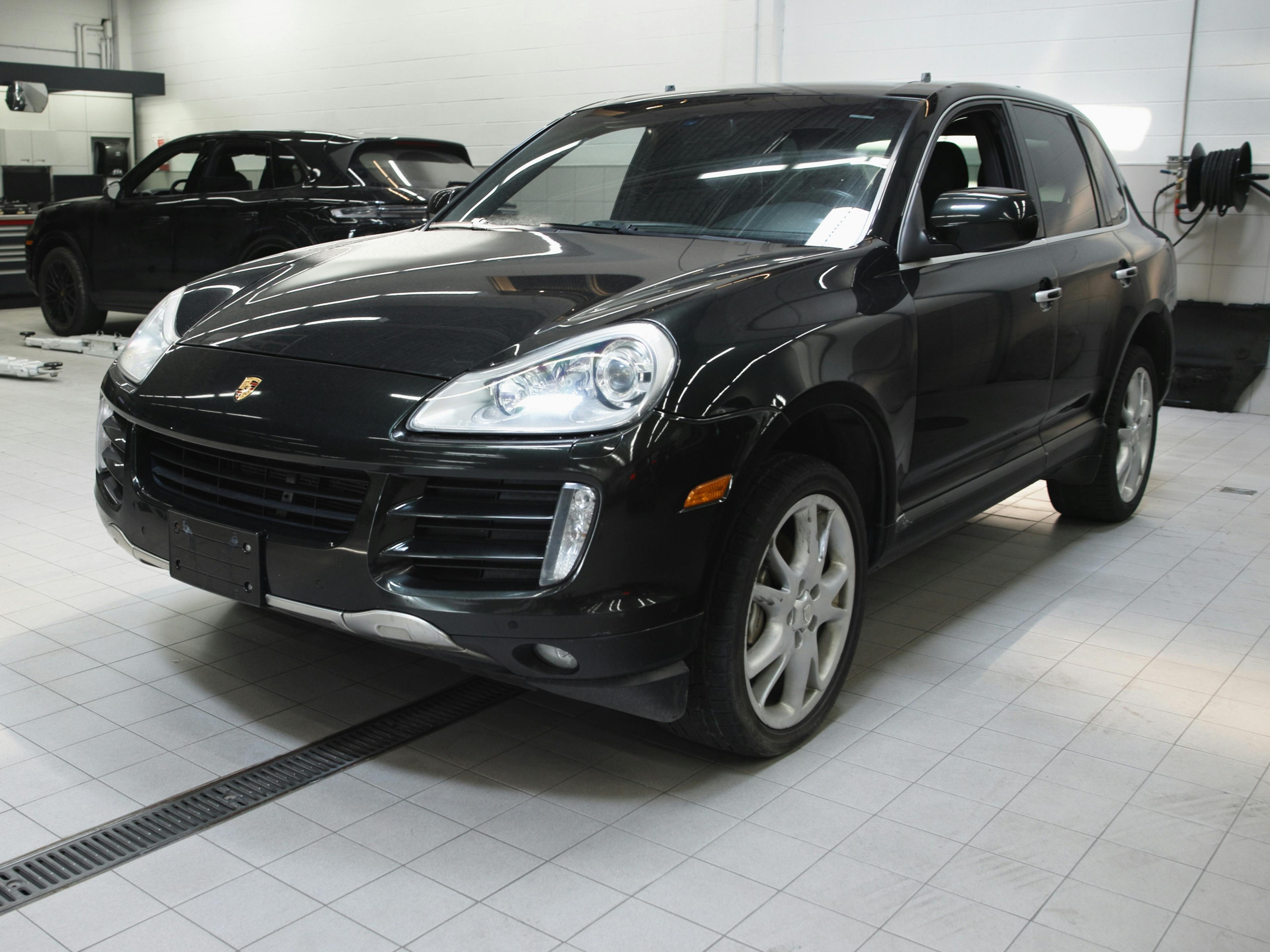 Oakville - A black Porsche Cayenne parked inside a workshop with other cars in the background.