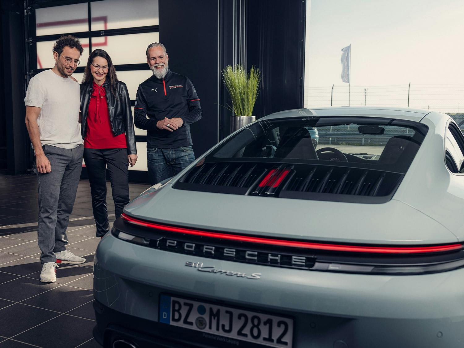 A couple taking delivery of a green Porsche 911 in a garage bay.