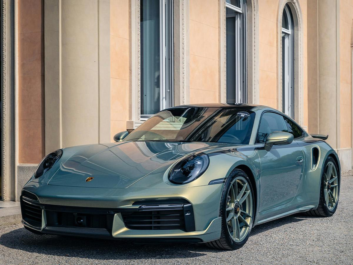 A 911 Turbo S in individual colour Urban Bamboo Chromaflair in front of a light orange house.
