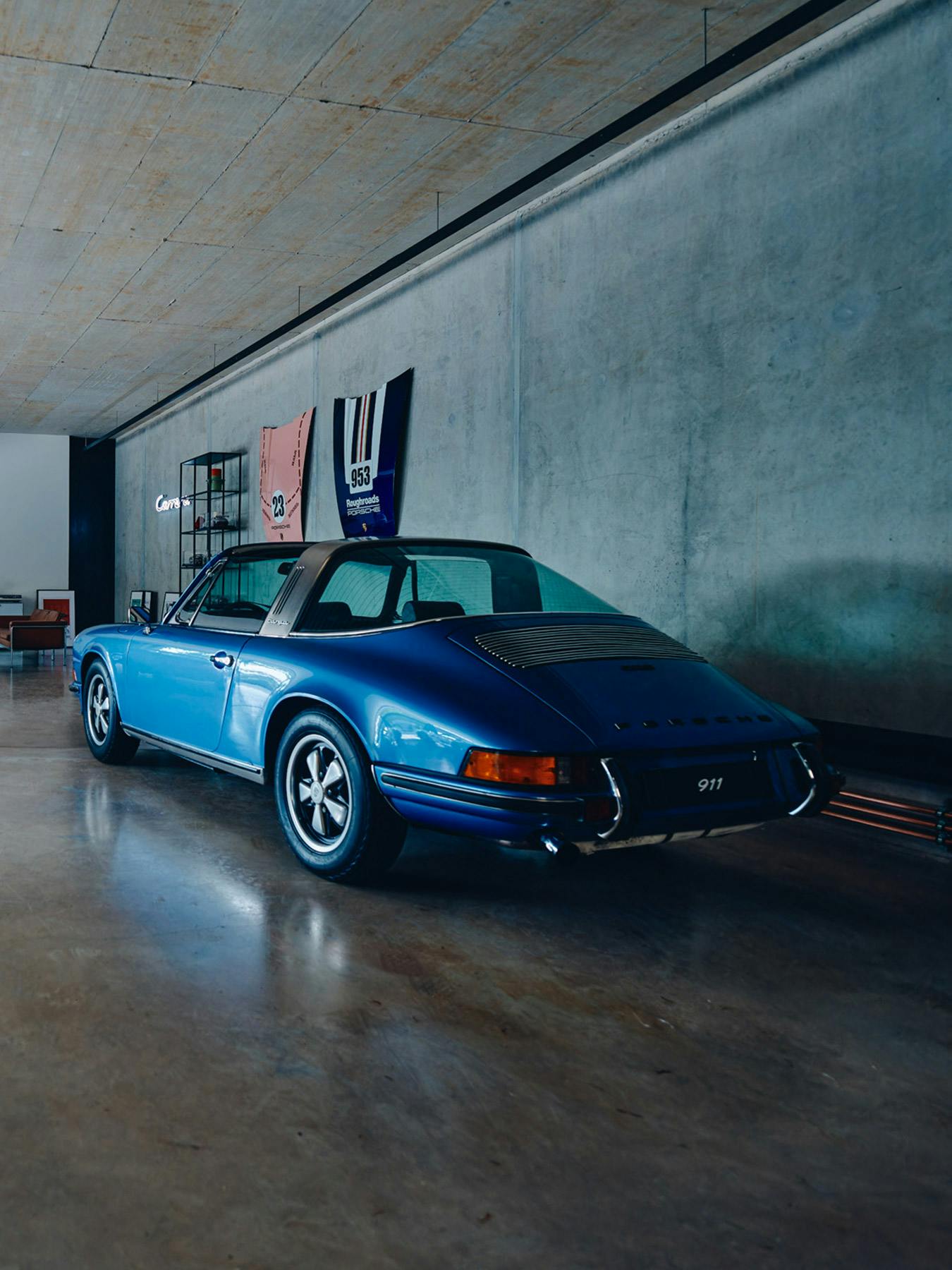 Porsche 911 Targa classique bleue dans un garage moderne avec des murs en béton et une décoration inspirée du sport automobile.
