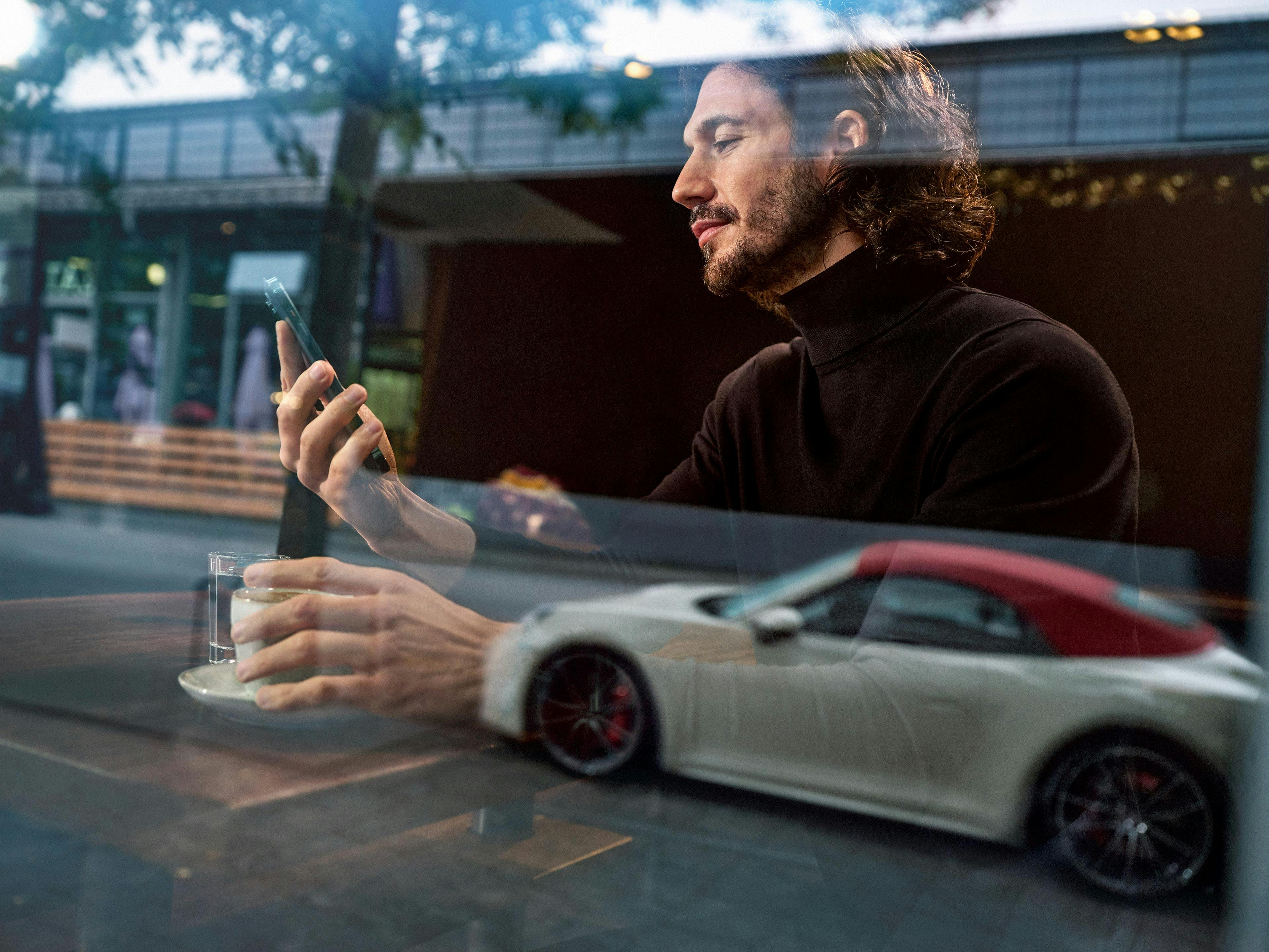Un uomo è seduto dietro una finestra e guarda il suo smartphone.