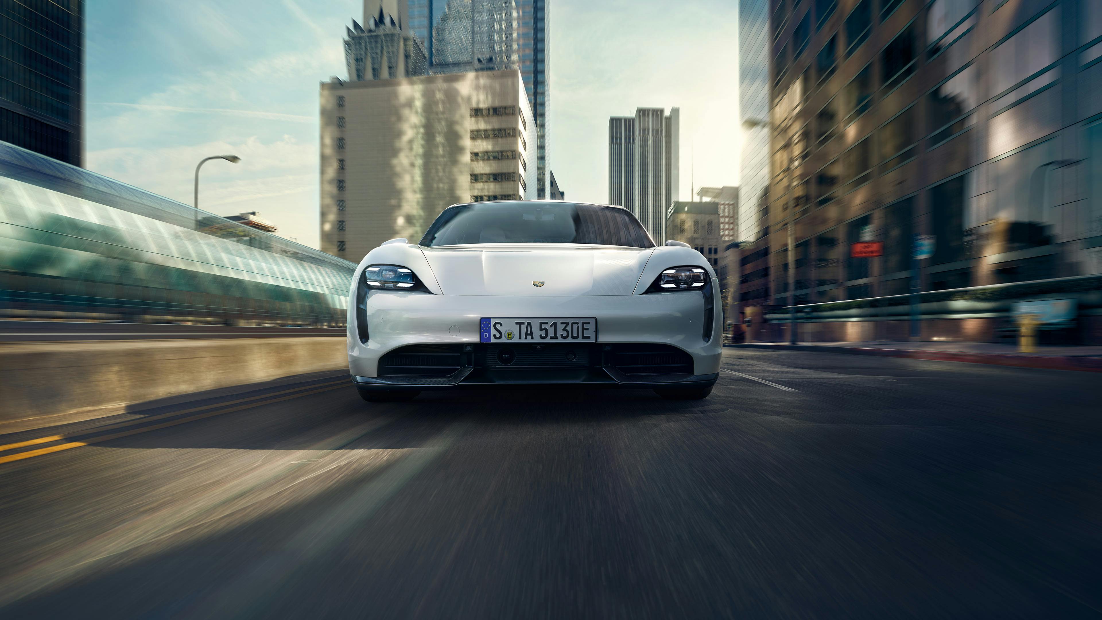 White Porsche Taycan driving on a city street.