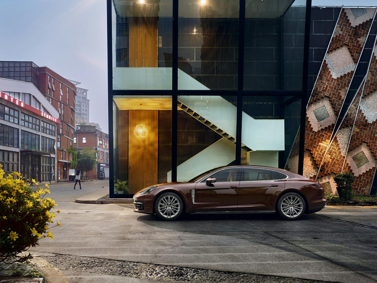 Ein Porsche Panamera vor modernem Gebäude mit Glasfassade und Treppe, umgeben von urbaner Architektur und Pflanzen.