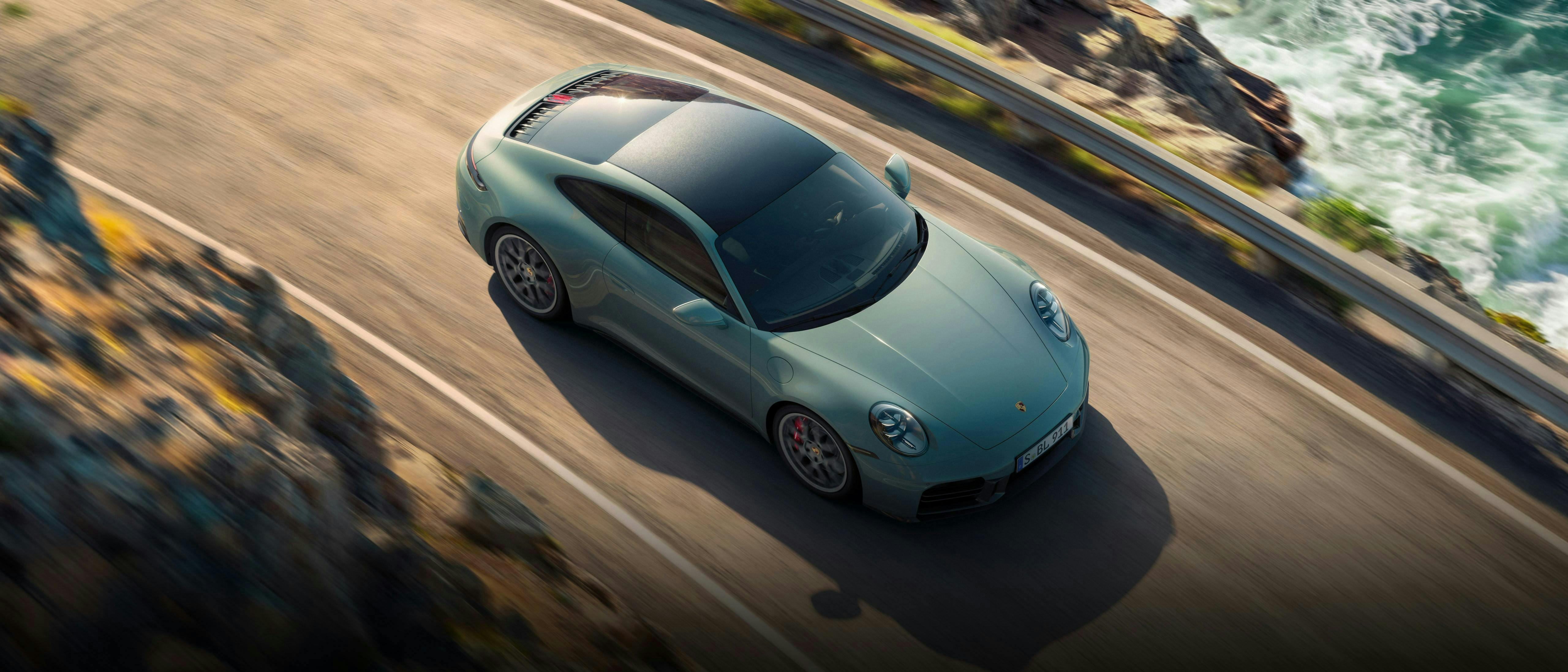 A light green Porsche 911 driving alongside a coastline.