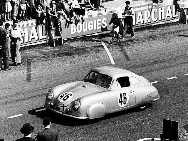 Porsche 356 SL mit Startnummer 46 fährt auf Rennstrecke; Zuschauende hinter Barriere mit Reklameschildern, Schwarz‑Weiß, frühe 1950er.