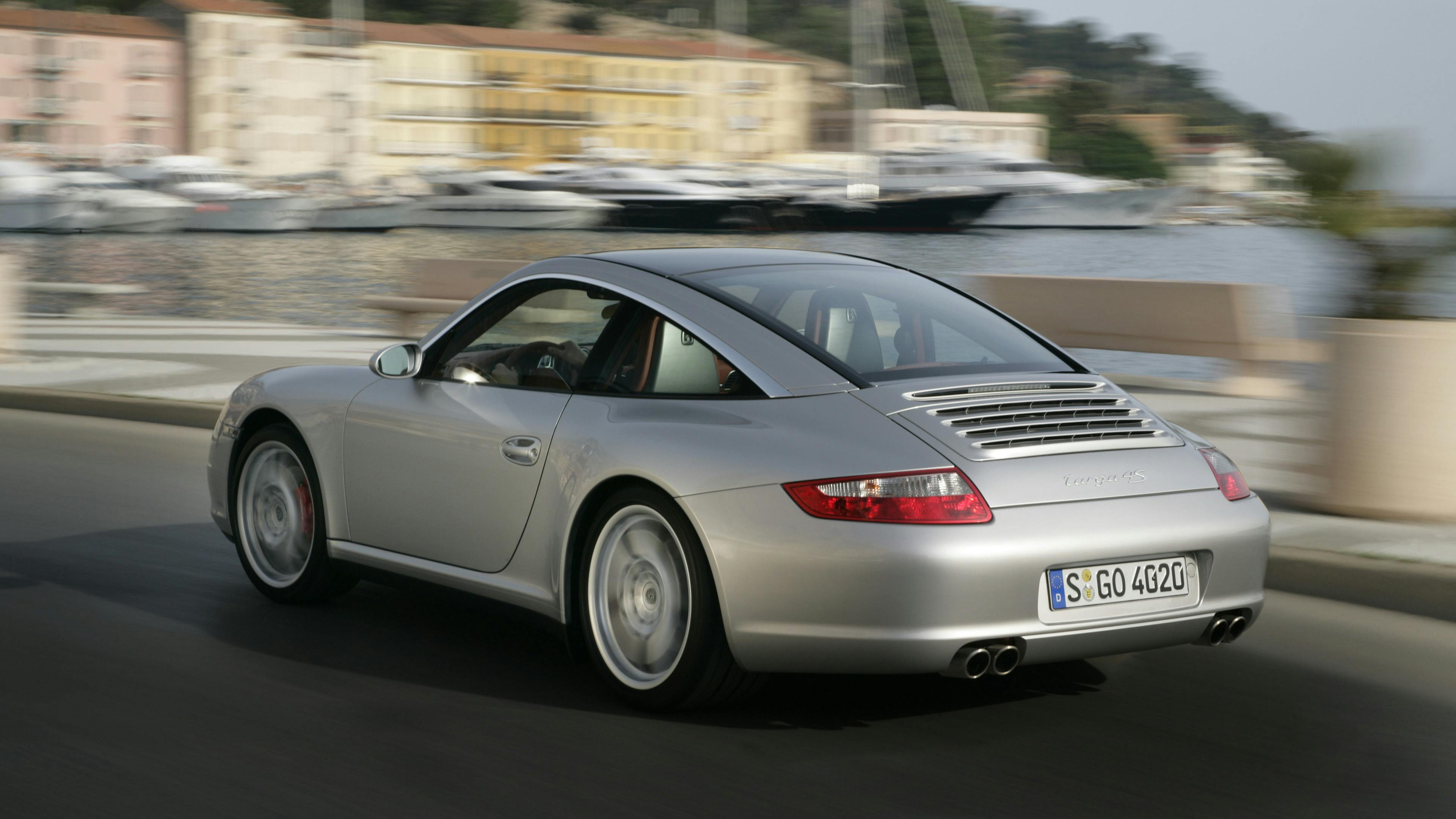 Driving silver 911 Targa 4S of the type 997 in a marina.