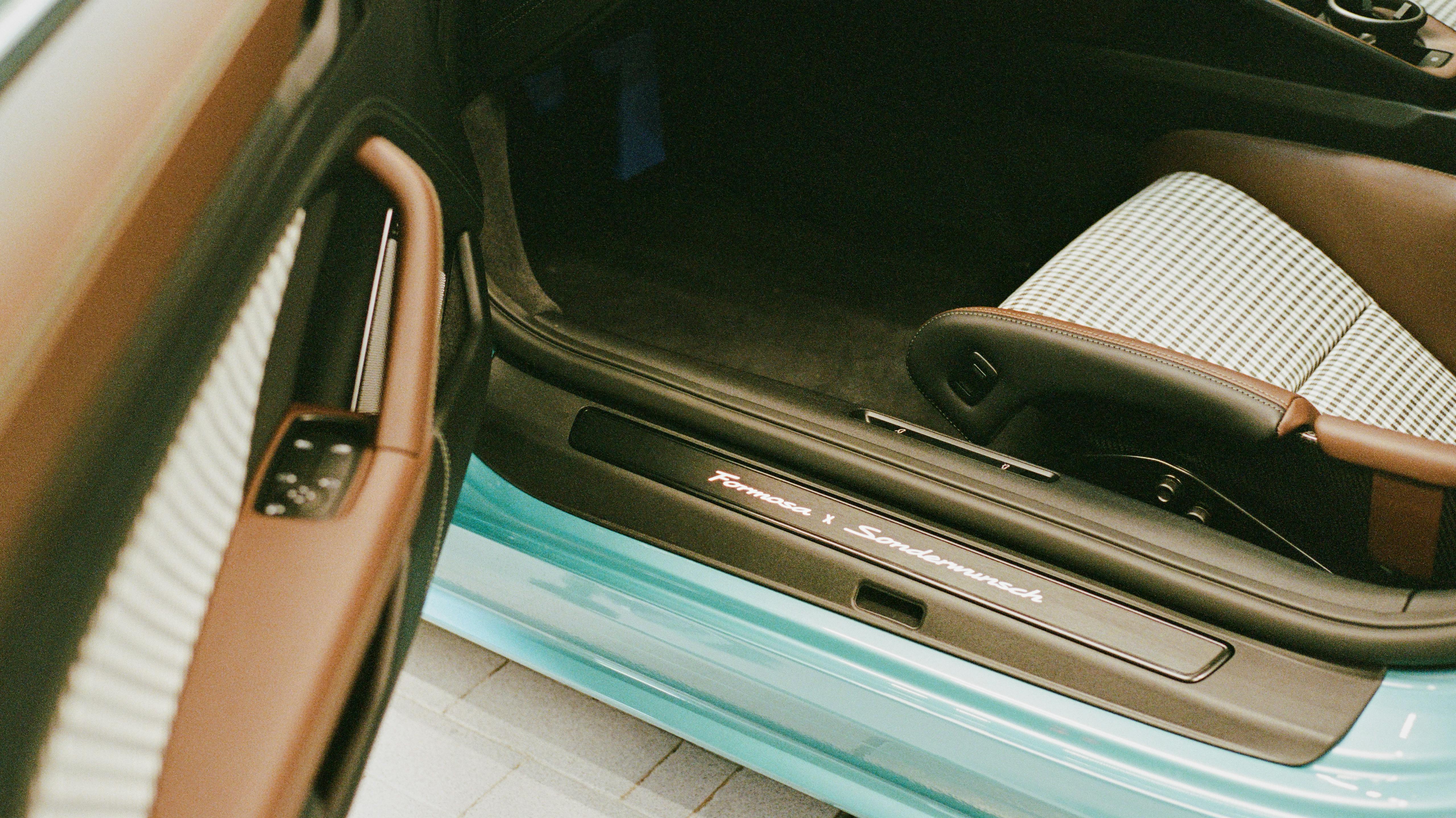 Detail of a turquoise Porsche 911 Carrera door sill with “Sonderwunsch” lettering and seat with classic check pattern.