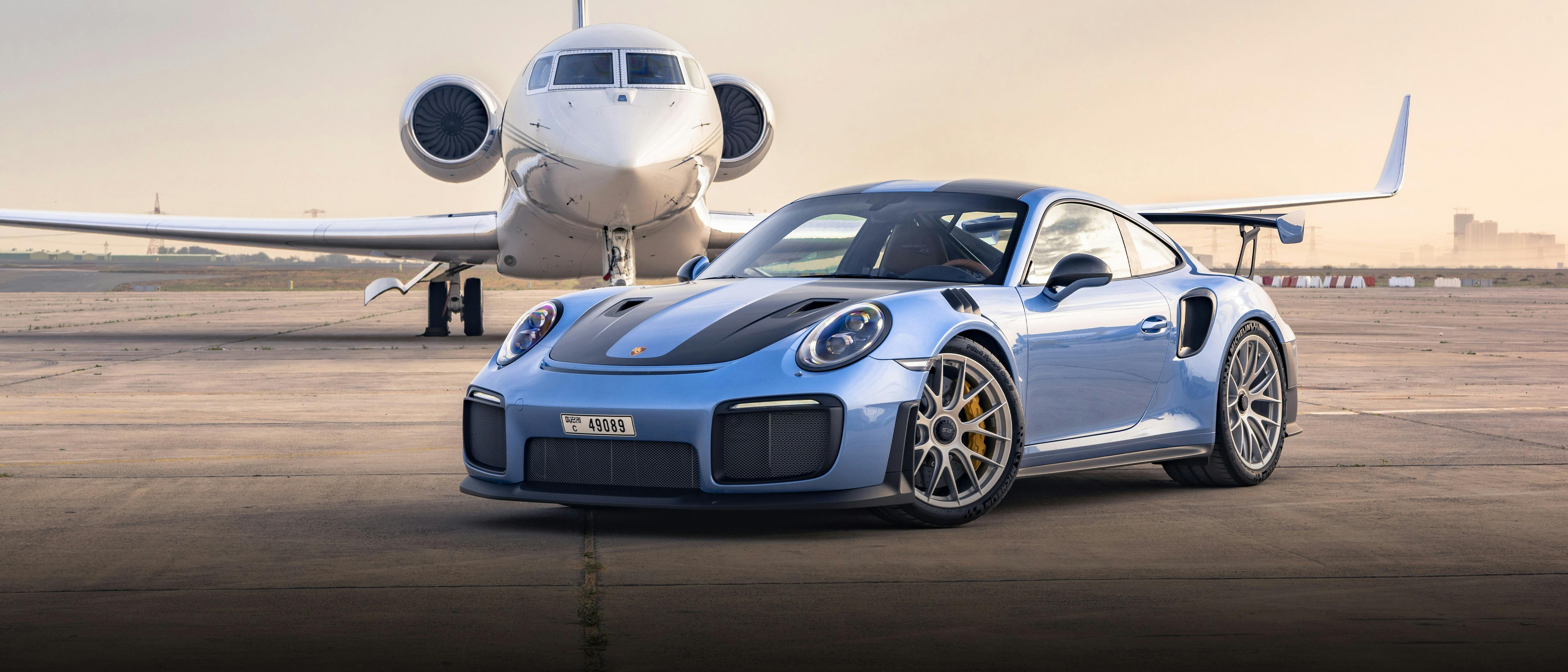 A 911 GT2 RS coloured in Geminimetallic in the left front of a small airplane on the tarmac.