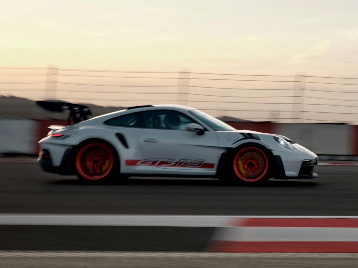 Une Porsche 911 GT3 RS blanche roulant à grande vitesse sur un circuit automobile, au crépuscule.