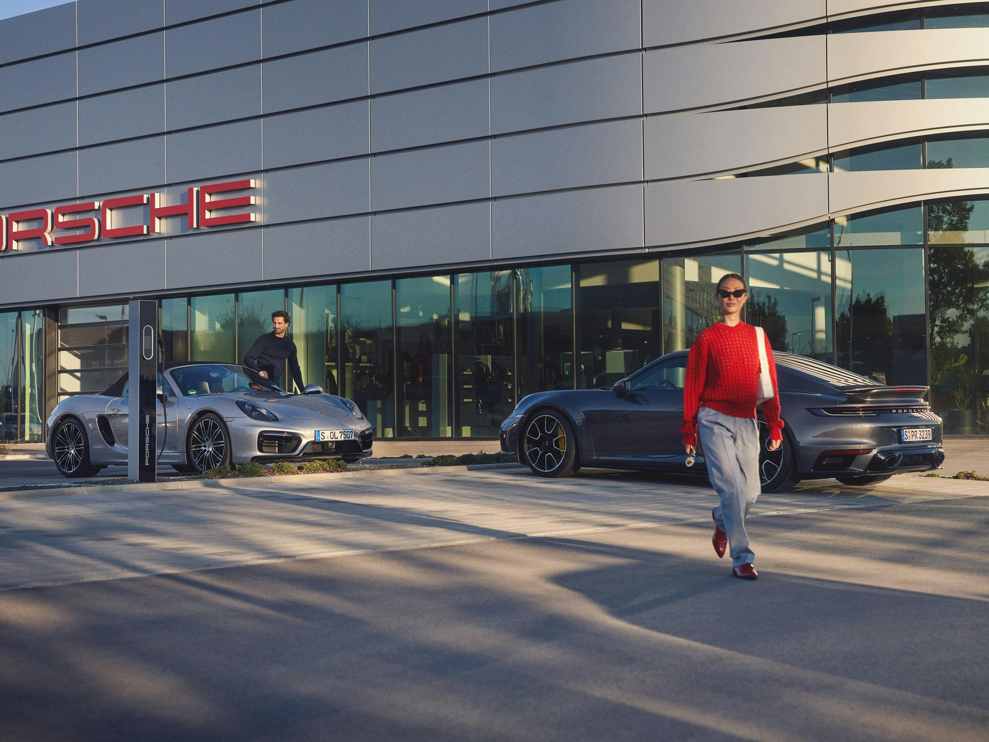 Two people getting out of their vehicle in front of a Porsche dealership.