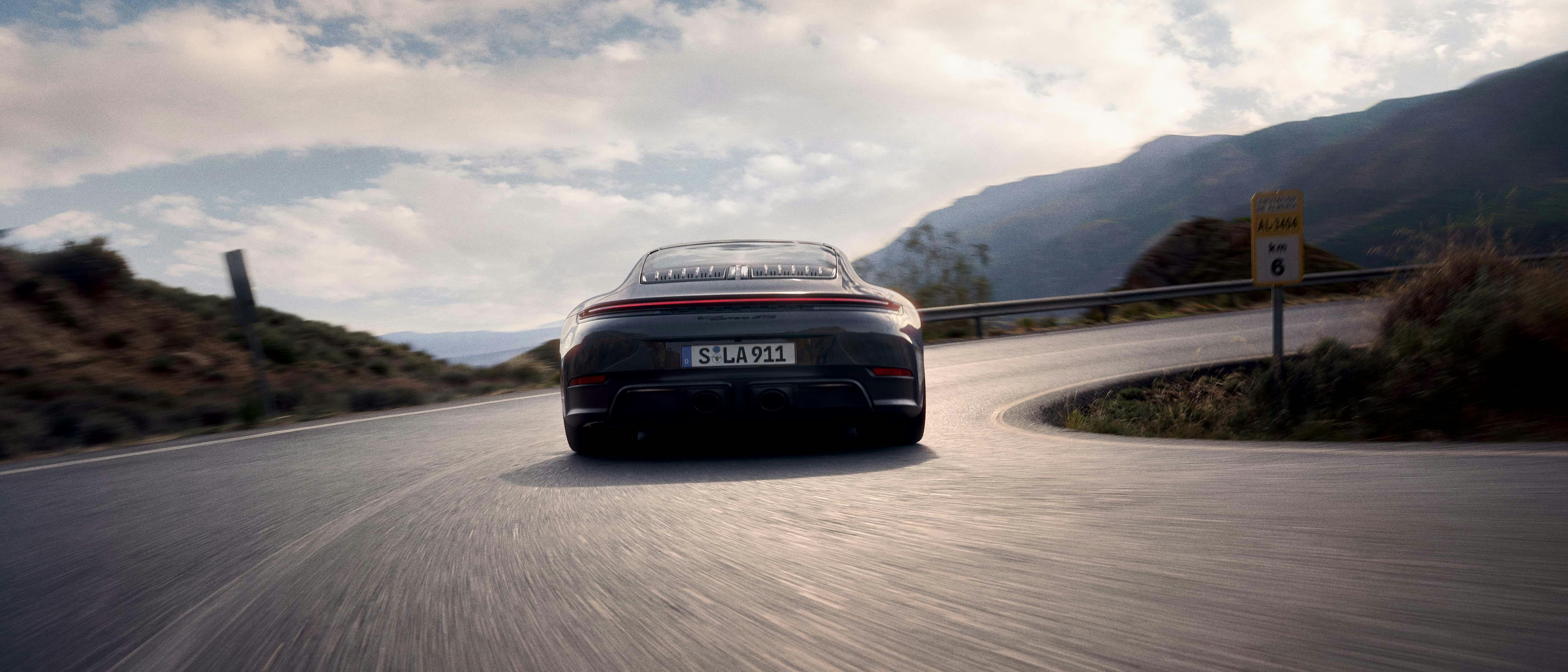 Porsche 911 GTS rijd over een bochtige weg tussen de bergen.