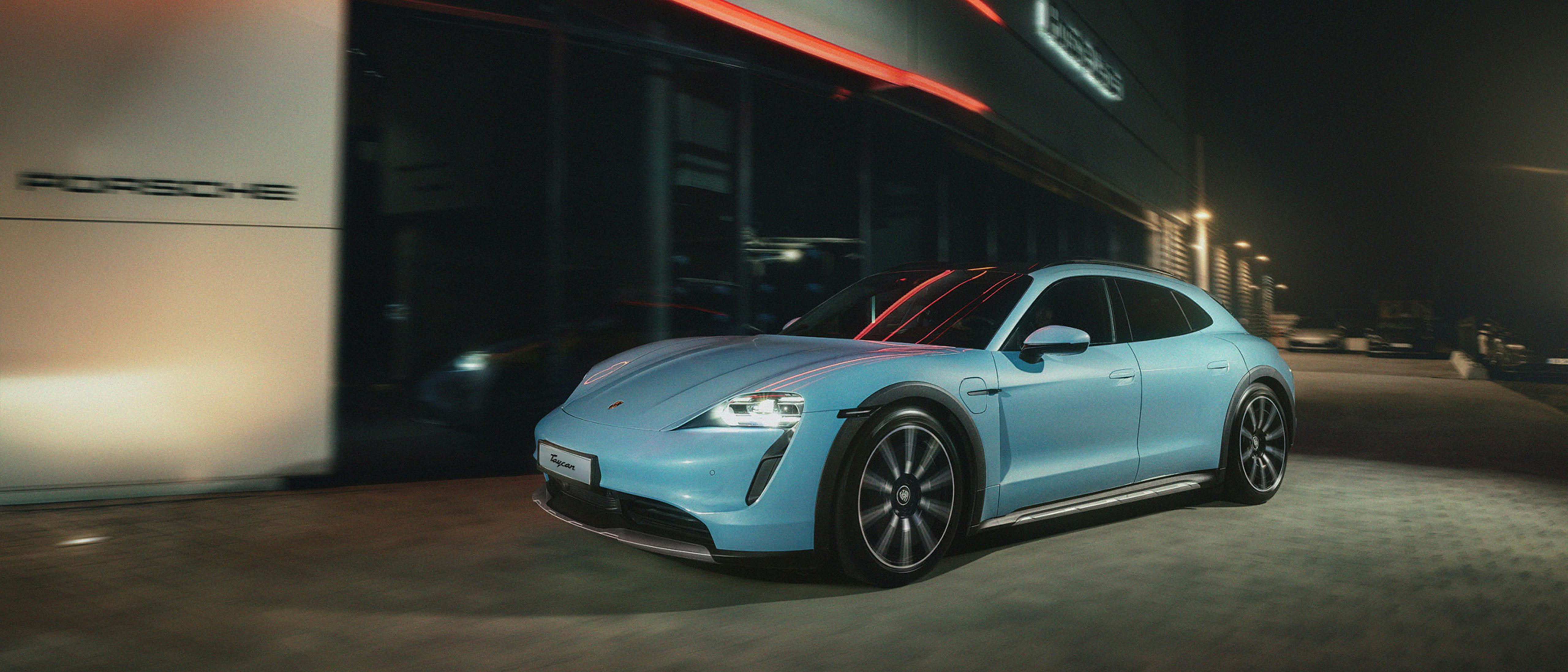 A light blue Porsche Taycan is parked outside a modern building at night, illuminated by red and white lights.