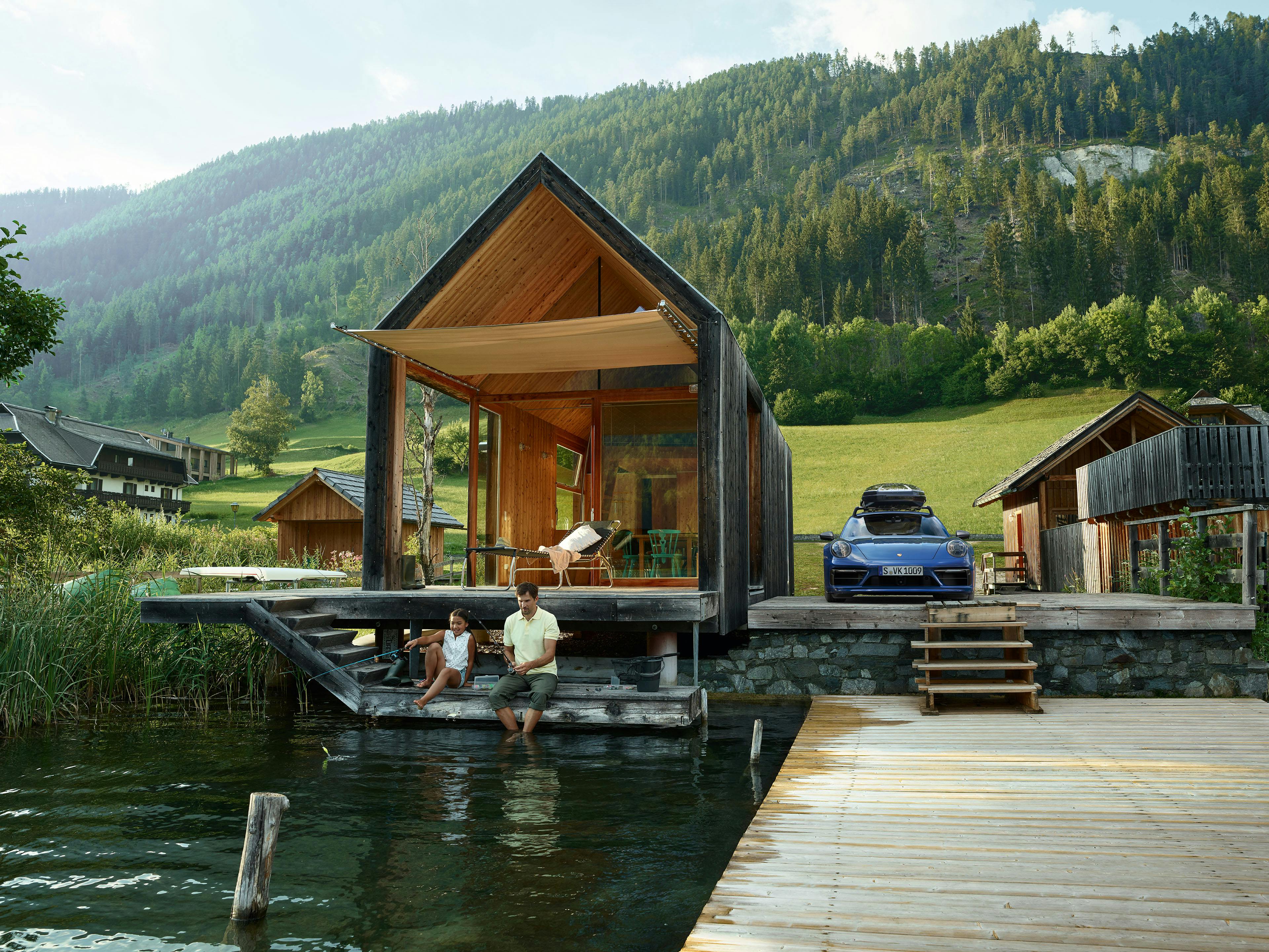 Idyllisches Haus am See mit Vater, Kind und einem blauen 911 Carrera 4S.