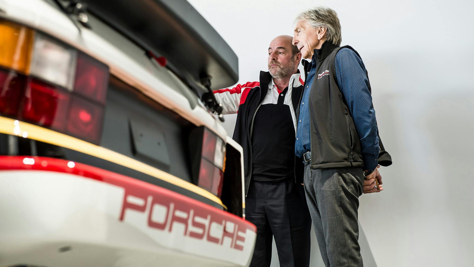 Employee standing next to a man, explaining something about the fully restored Porsche 924 GTP.