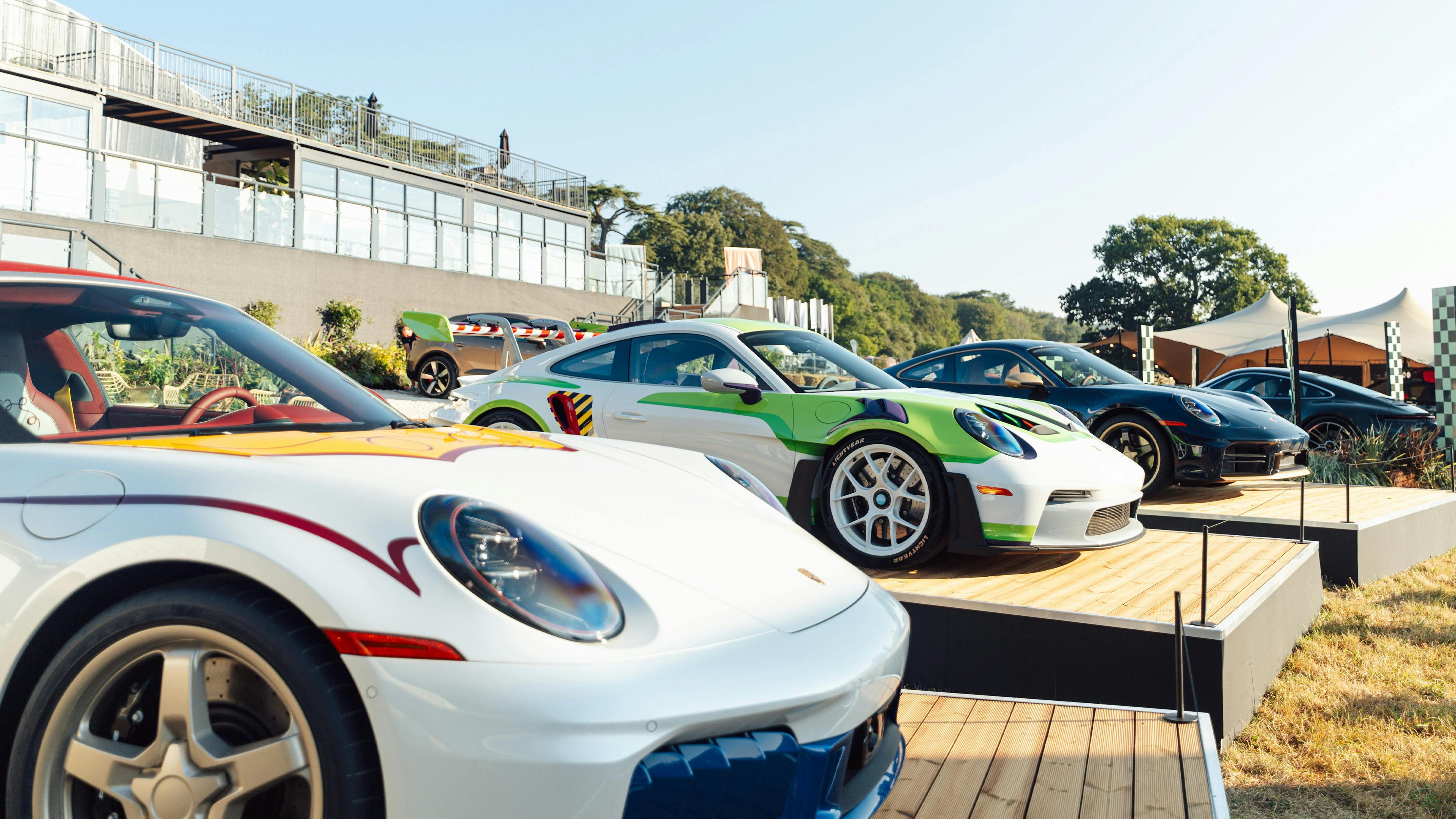 A line-up of colourfully liveried Porsche 911 GT3s Toy Story cars displayed on a wooden platform at Goodwood Festival of Speed.