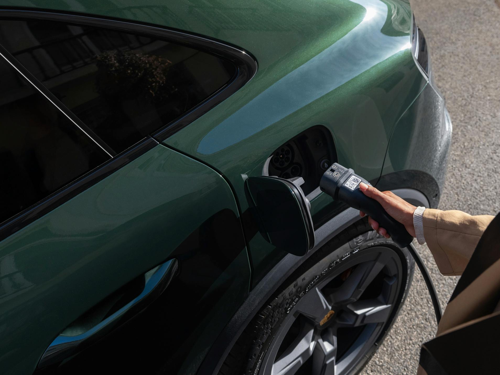 A person plugging a charging plug into the charging socket of a Porsche Macan 4S.