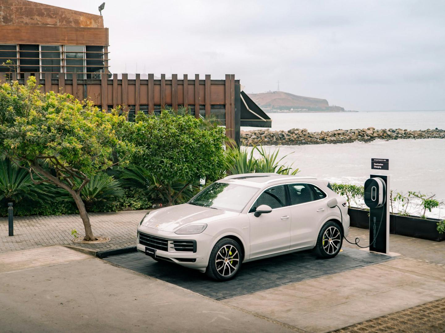 White Porsche Cayenne E-Hybrid charging at destination charging station outside the Cala Restaurant in Lima with ocean view.