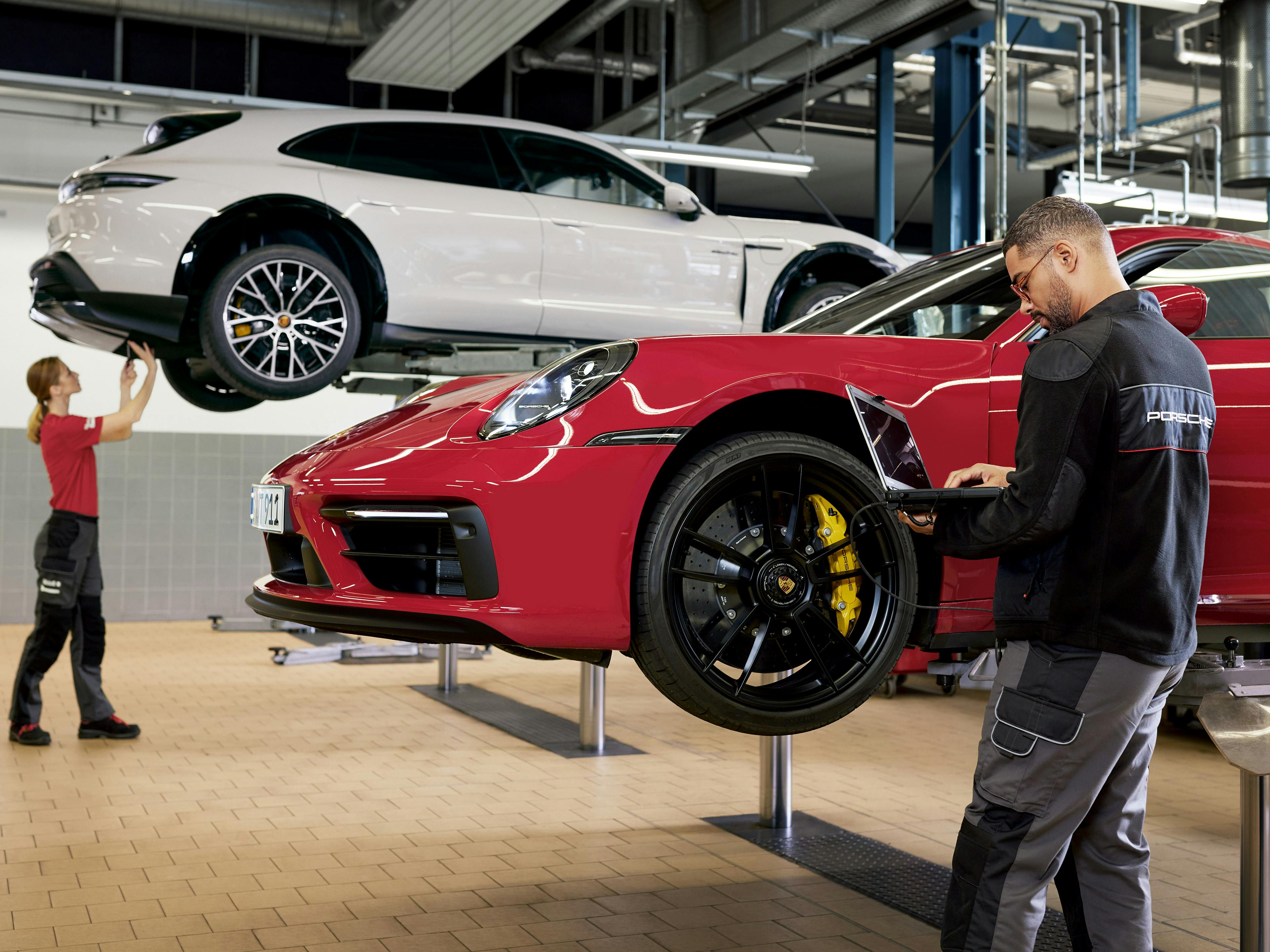 Un uomo e una donna lavorano in officina riparando una Porsche 911 rossa e una Porsche Taycan bianca