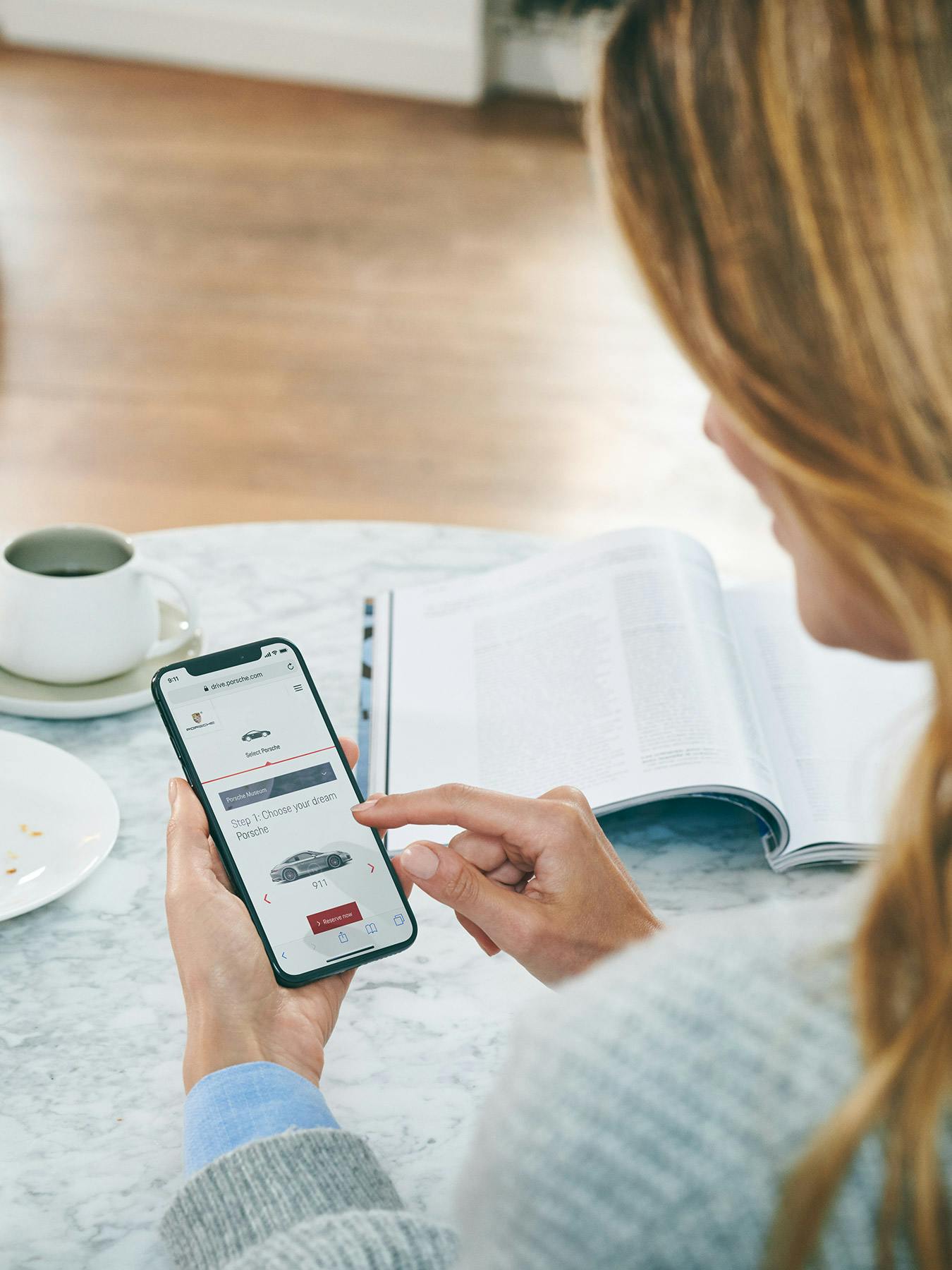 女性がコーヒーを飲みながら小さな丸テーブルに座り、携帯電話で記事を読んでいる。