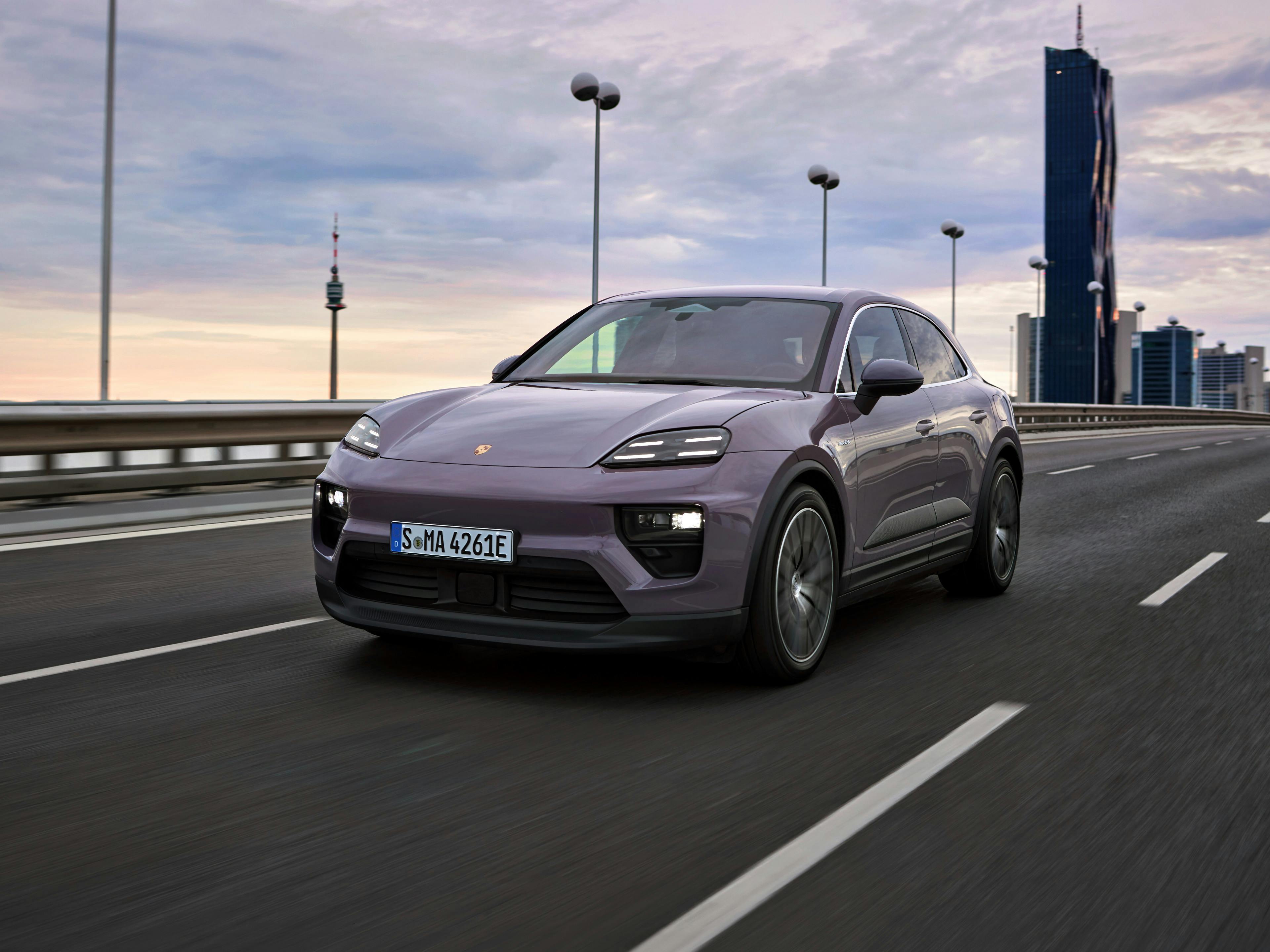 A Macan 4 Electric in Provence driving across a long road, with tall buildings in the background.