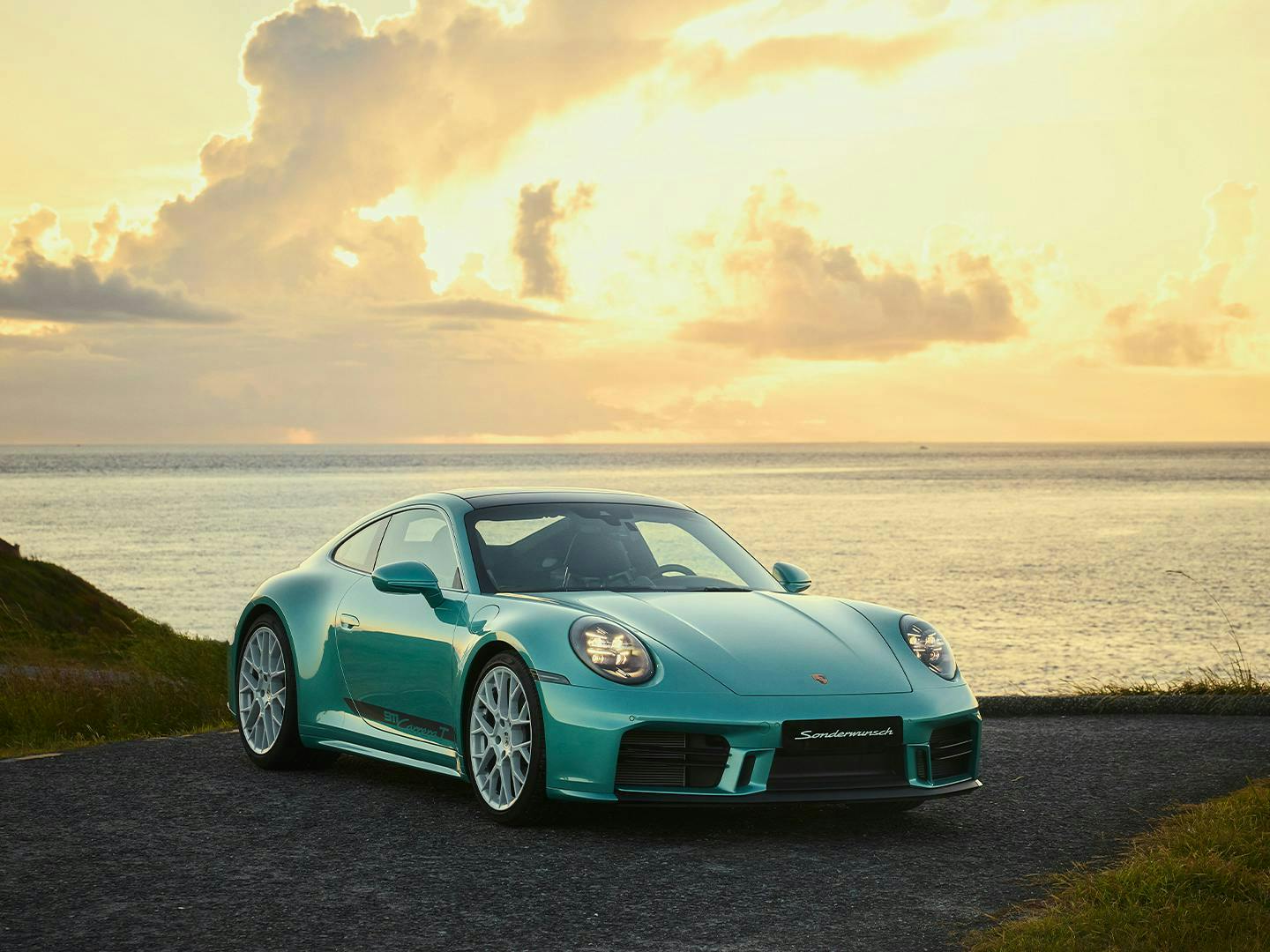 水綠色 Porsche 911 Carrera 停在海岸公路上的細節照，夕陽下的前視圖，可見前大燈。