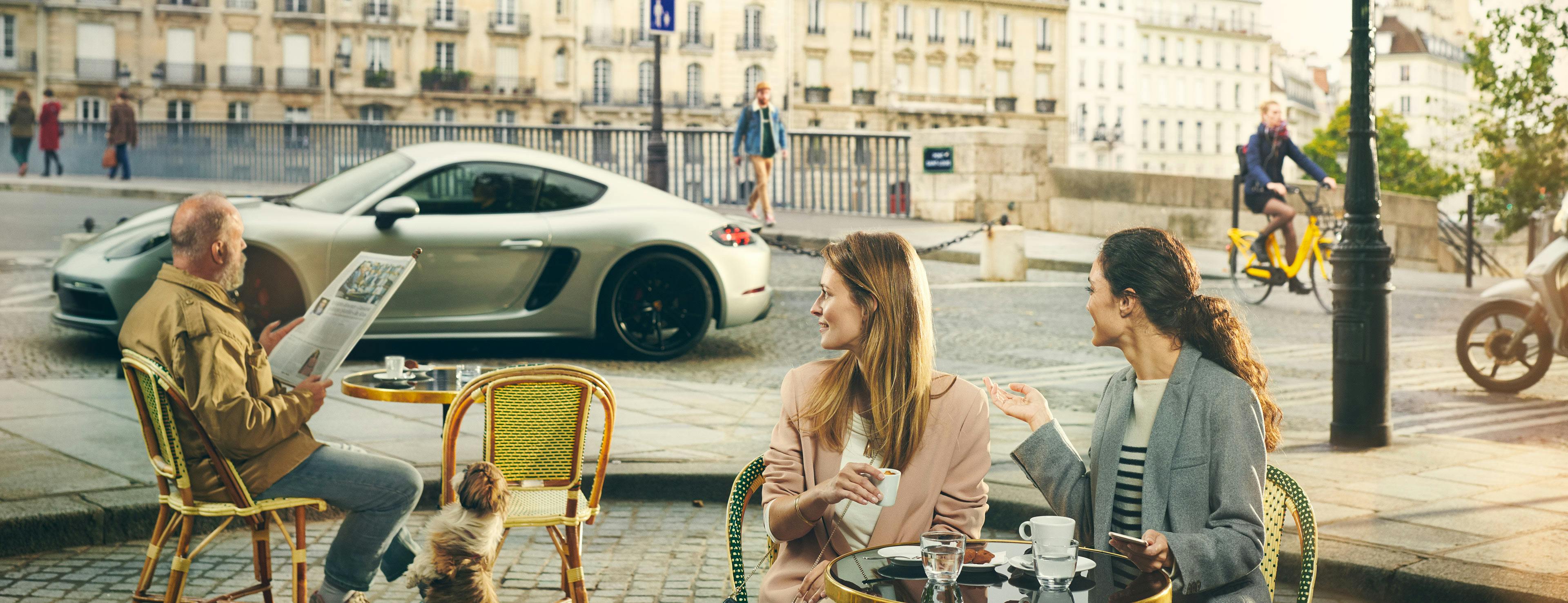 A Porsche Taycan in a city scene, several people are sitting at tables in the front.