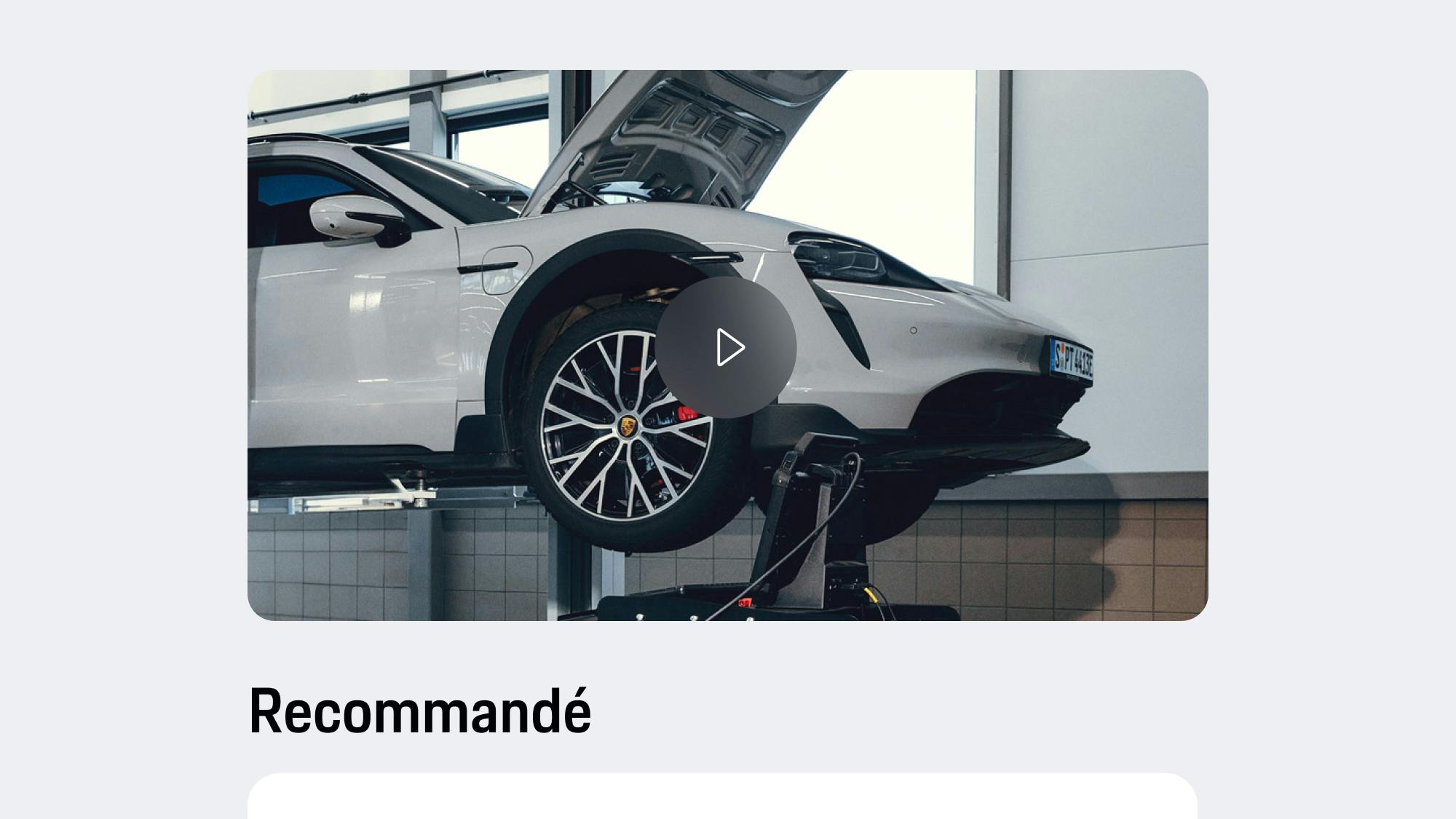 Vue de l'application montrant une Porsche gris clair sur un pont élévateur avec le capot ouvert, un bouton de lecture vidéo et un texte de recommandation affiché en dessous.