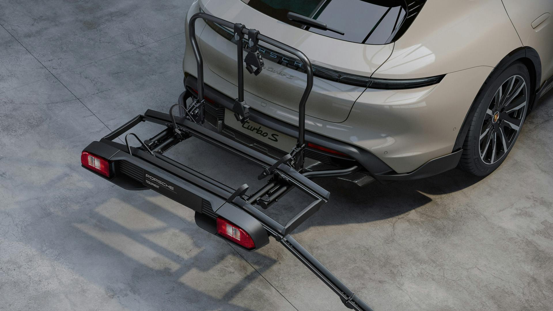 Rear view of a beige Porsche Taycan Turbo S with a mounted rear bike carrier system in a clean, modern garage setting.