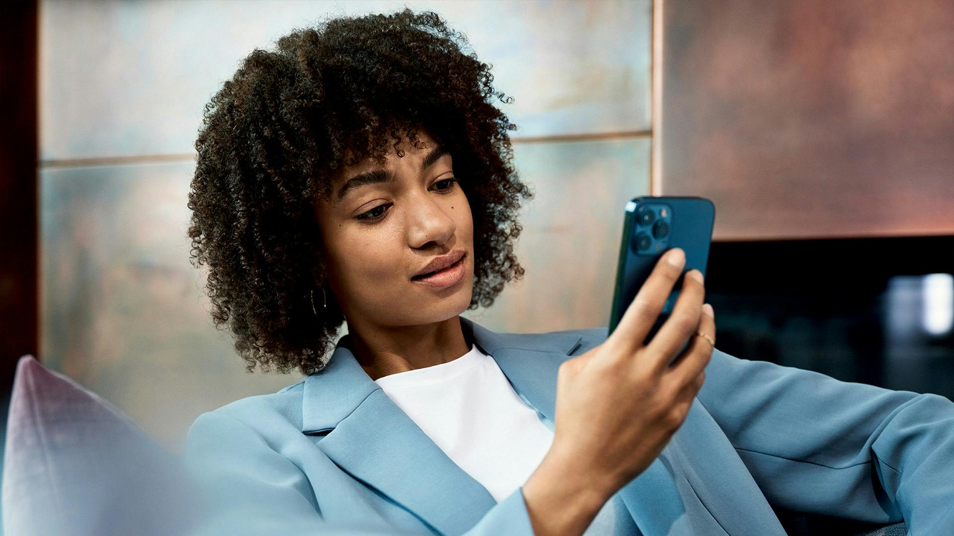 Une femme en costume bleu tient un téléphone portable à la main.