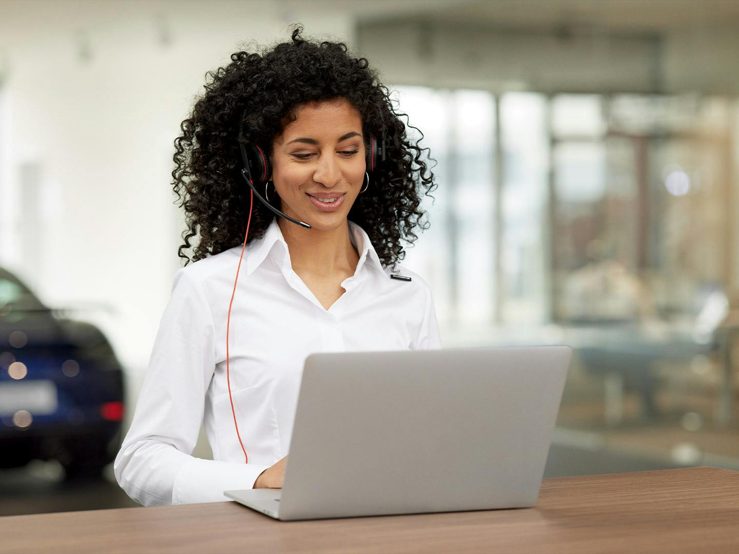 Un'assistente del servizio Porsche è impegnata in una conversazione in cuffia e sta guardando il suo computer portatile.