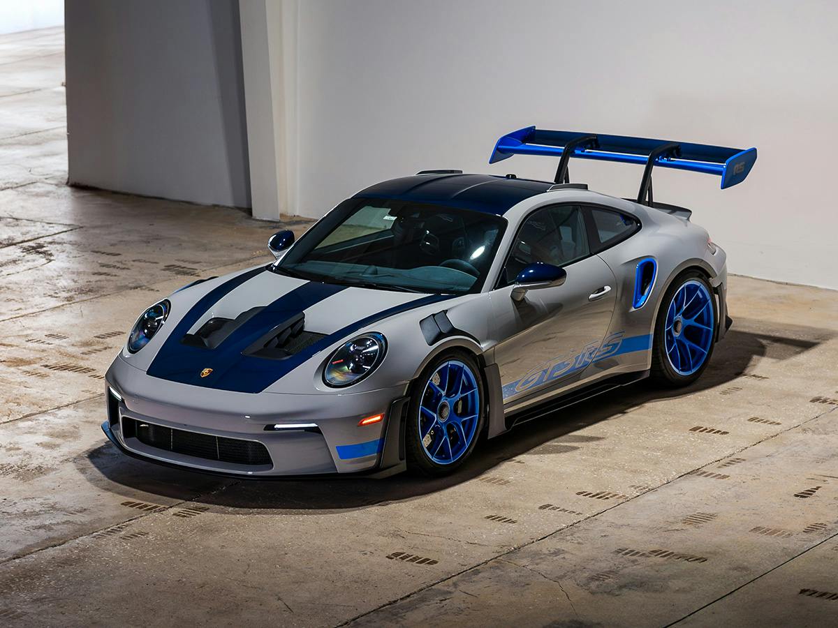 Porsche 911 GT3 RS in silver-blue with large rear wing on concrete floor.
