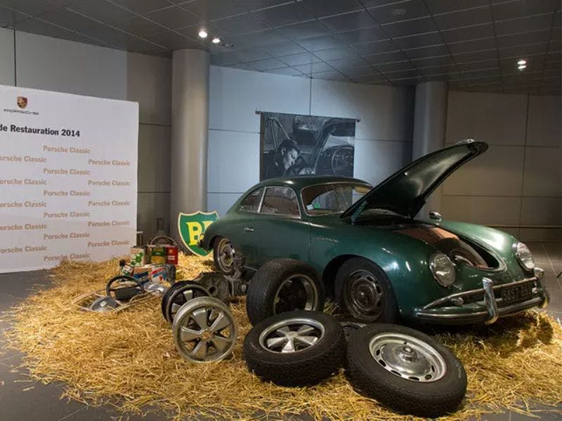 Le véhicule restauré se trouve sur une surface d'exposition dans le foin. Le capot avant est ouvert et des pneus et des jantes sont posés à côté.