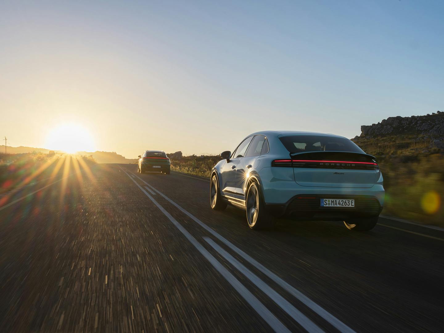 Πίσω άποψη της Macan εν κινήσει σε ανοιχτό δρόμο με την ανεγειρόμενη, η οποία ακολουθεί μία όμοια Macan, σε κατάσταση ηλιοβασιλέματος.
