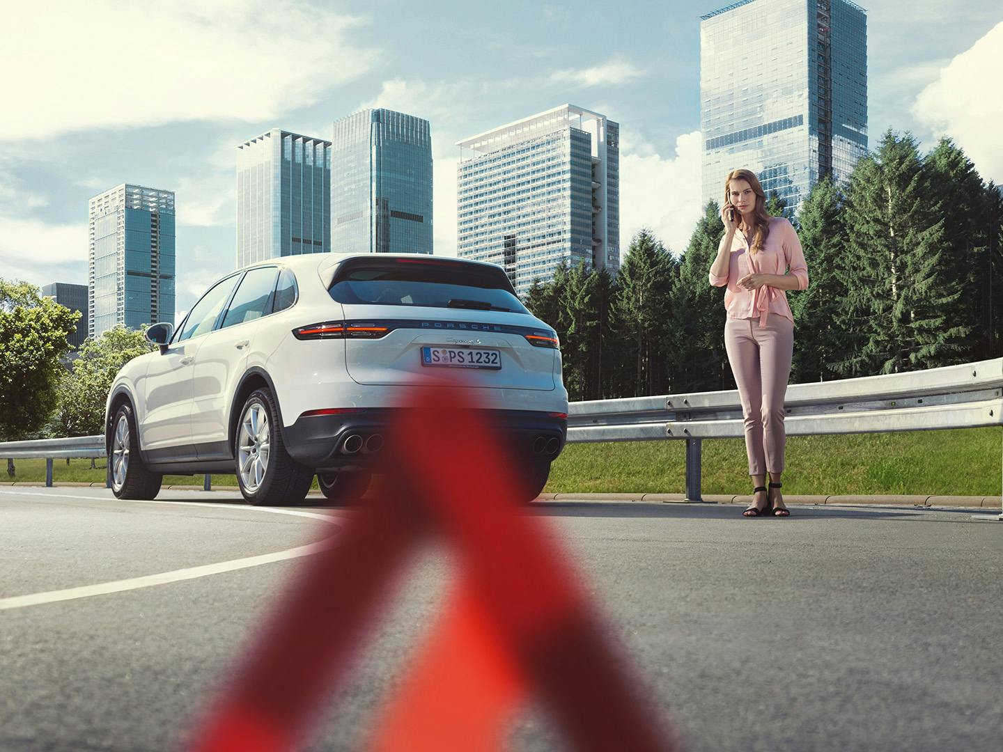 A woman stands by her vehicle on the roadside, looking concerned, with a city skyline in the background.