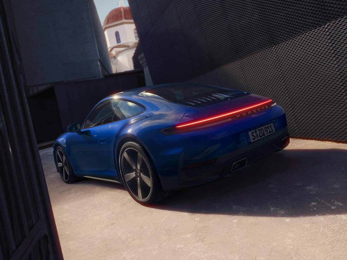 The 911 Carrera parked near a black fence. The Porsche light strip at the rear of the car is lit red.