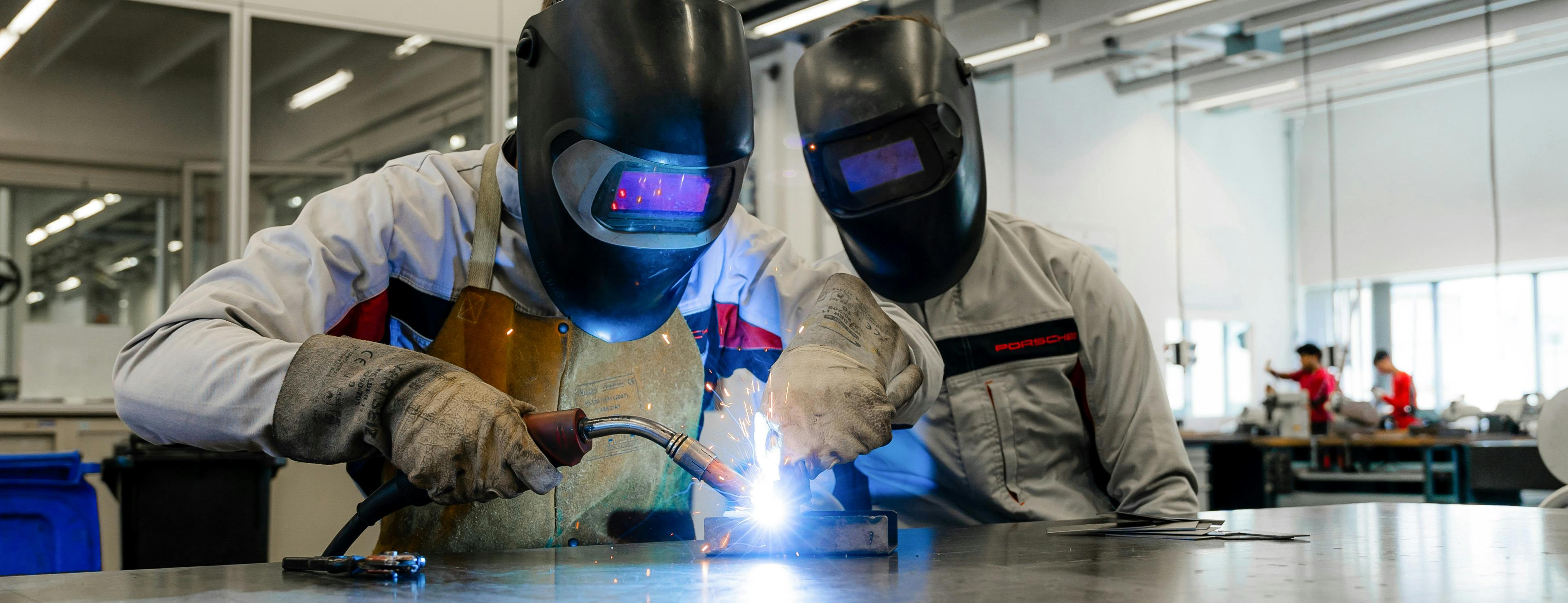 Zwei Porsche Auszubildende schweißen an einem Bauteil in der Werkstatt im Ausbildungszentrum.