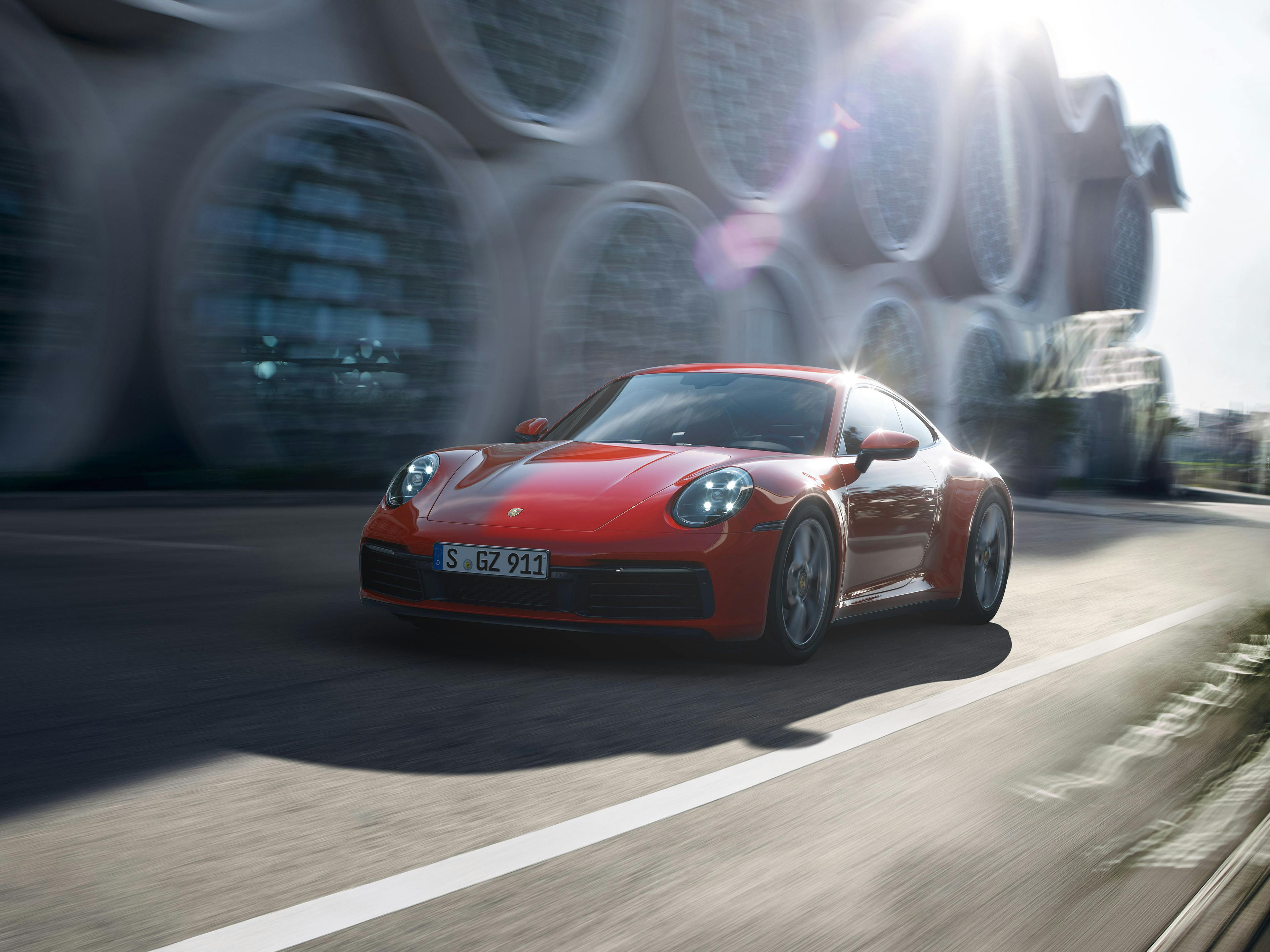 A red Porsche 911 cruising through the city on a bright sunny day.