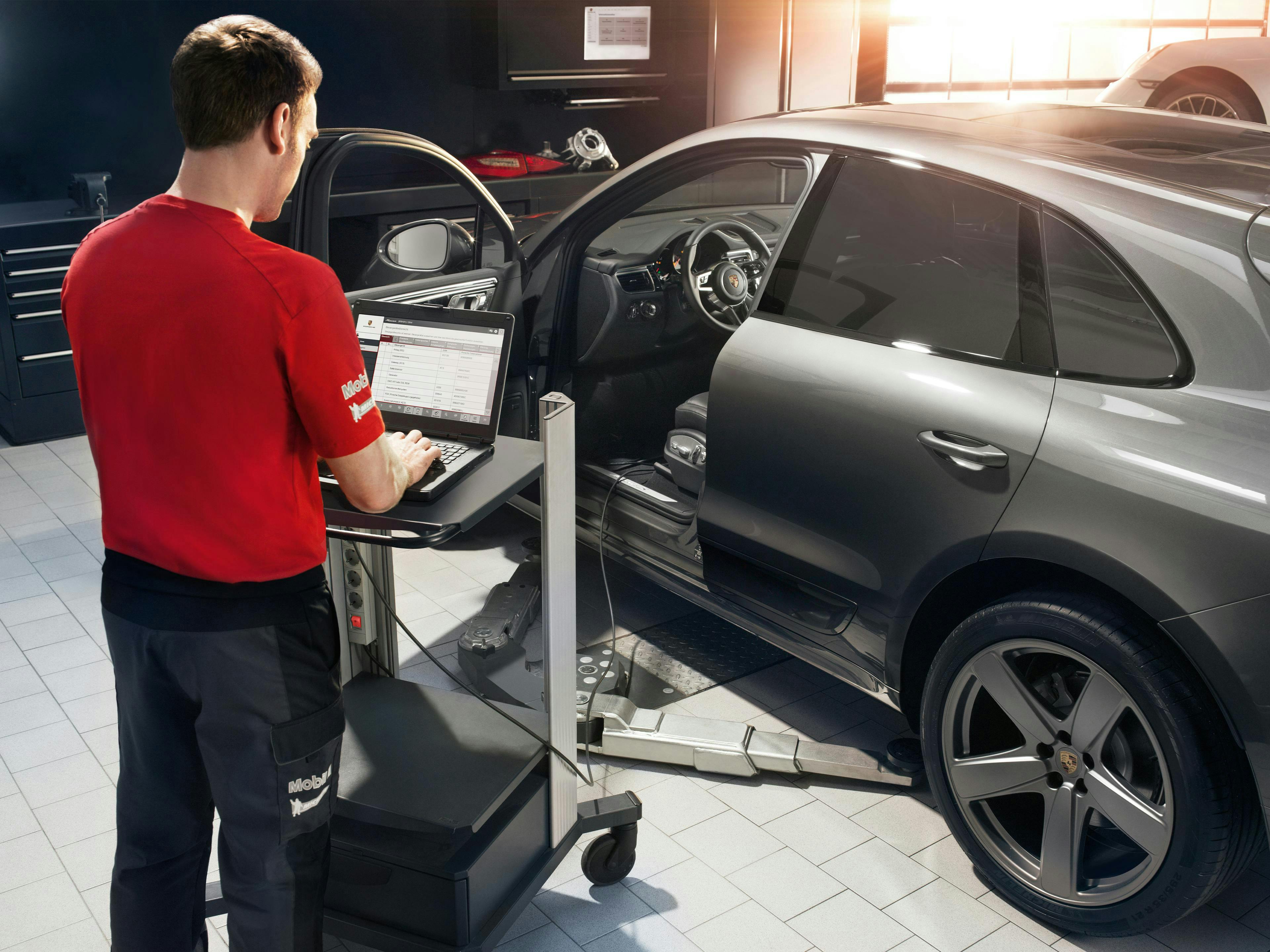 En tekniker jobber på en sølvgrå Porsche på et verksted.