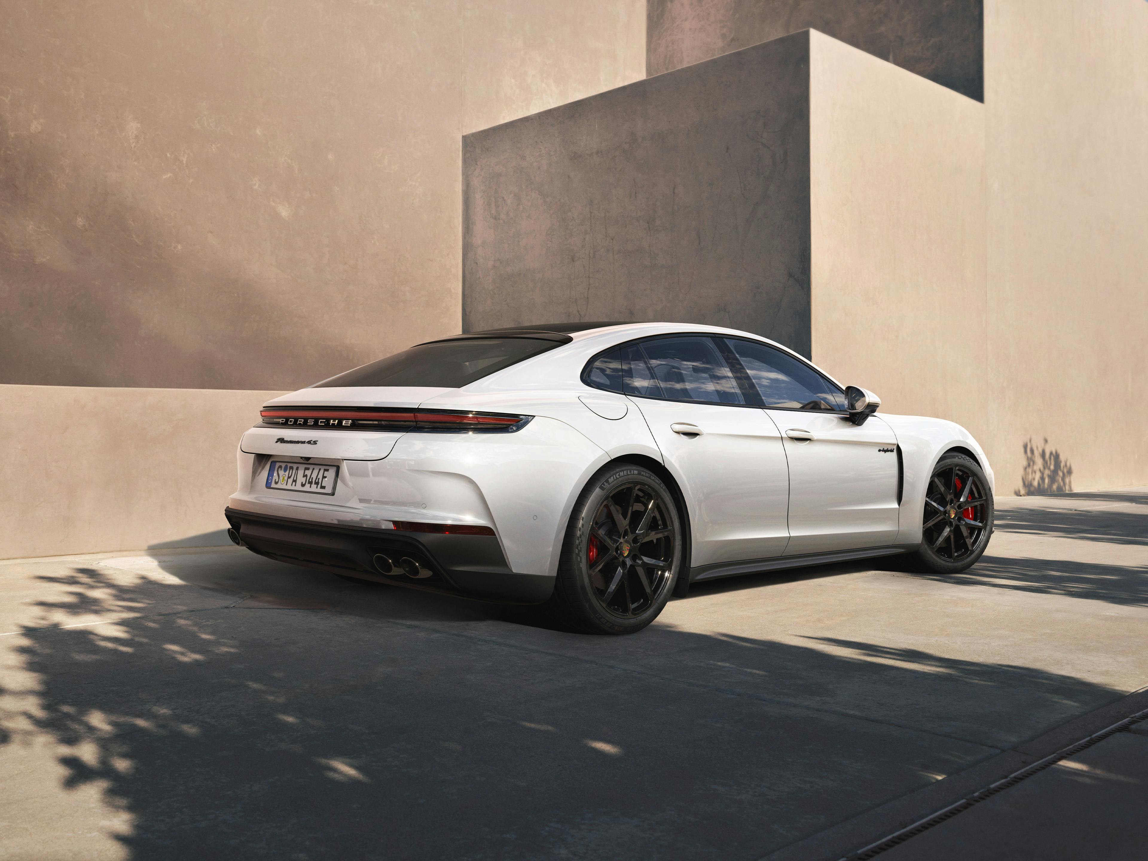 The Panamera 4S E-Hybrid parked near a stone coloured, modern building, with the shadows of a nearby tree in the foreground.