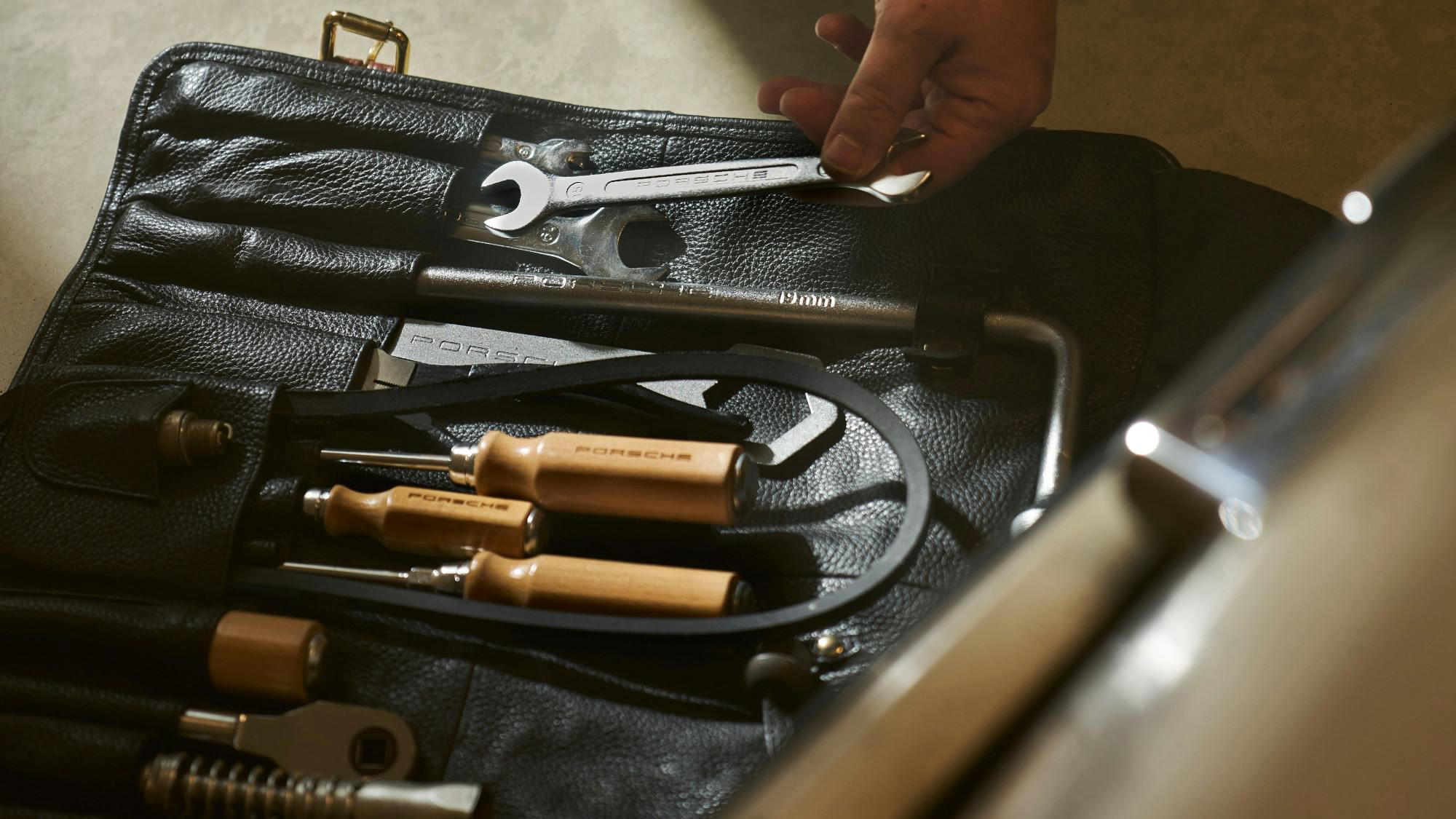 A hand placing a wrench into a Porsche toolkit.