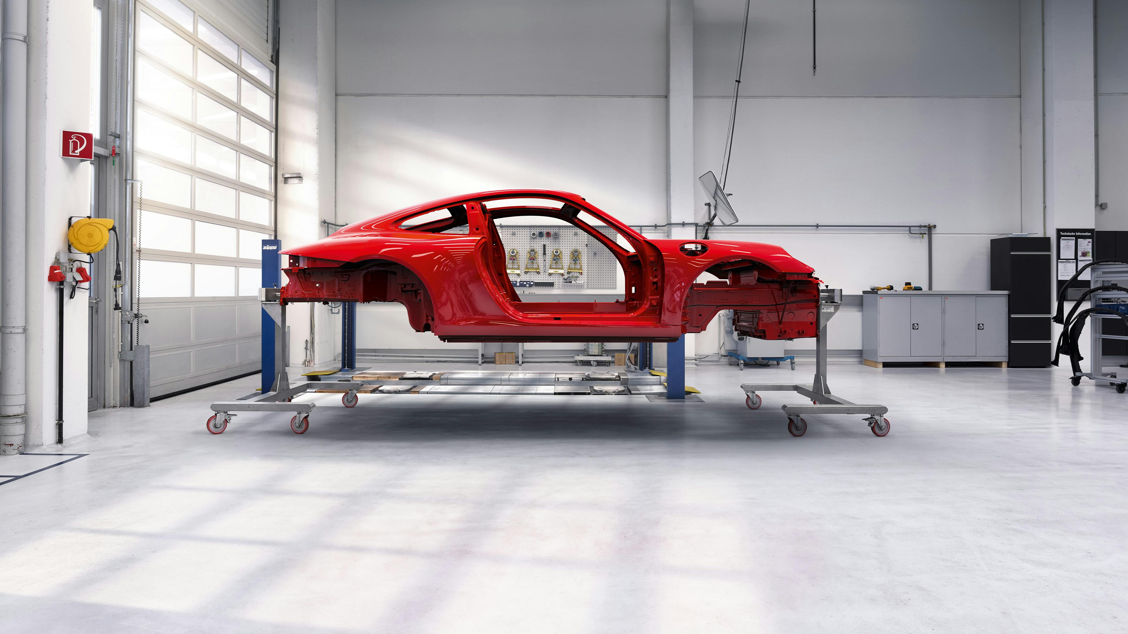 Red Porsche body on a frame in a workshop.