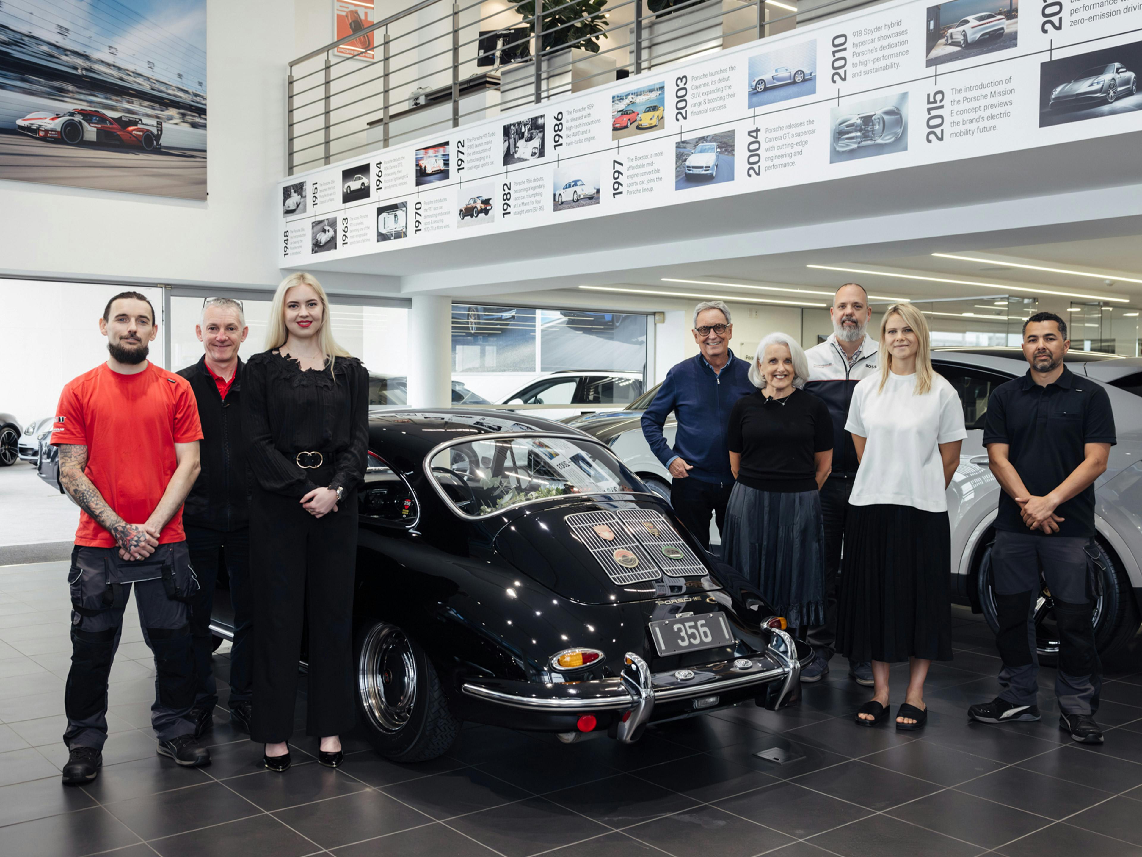The Porsche Classic Partner team and Deb Simpson stand next to the newly restored Porsche 356 in the showroom of Giltrap Porsche.
