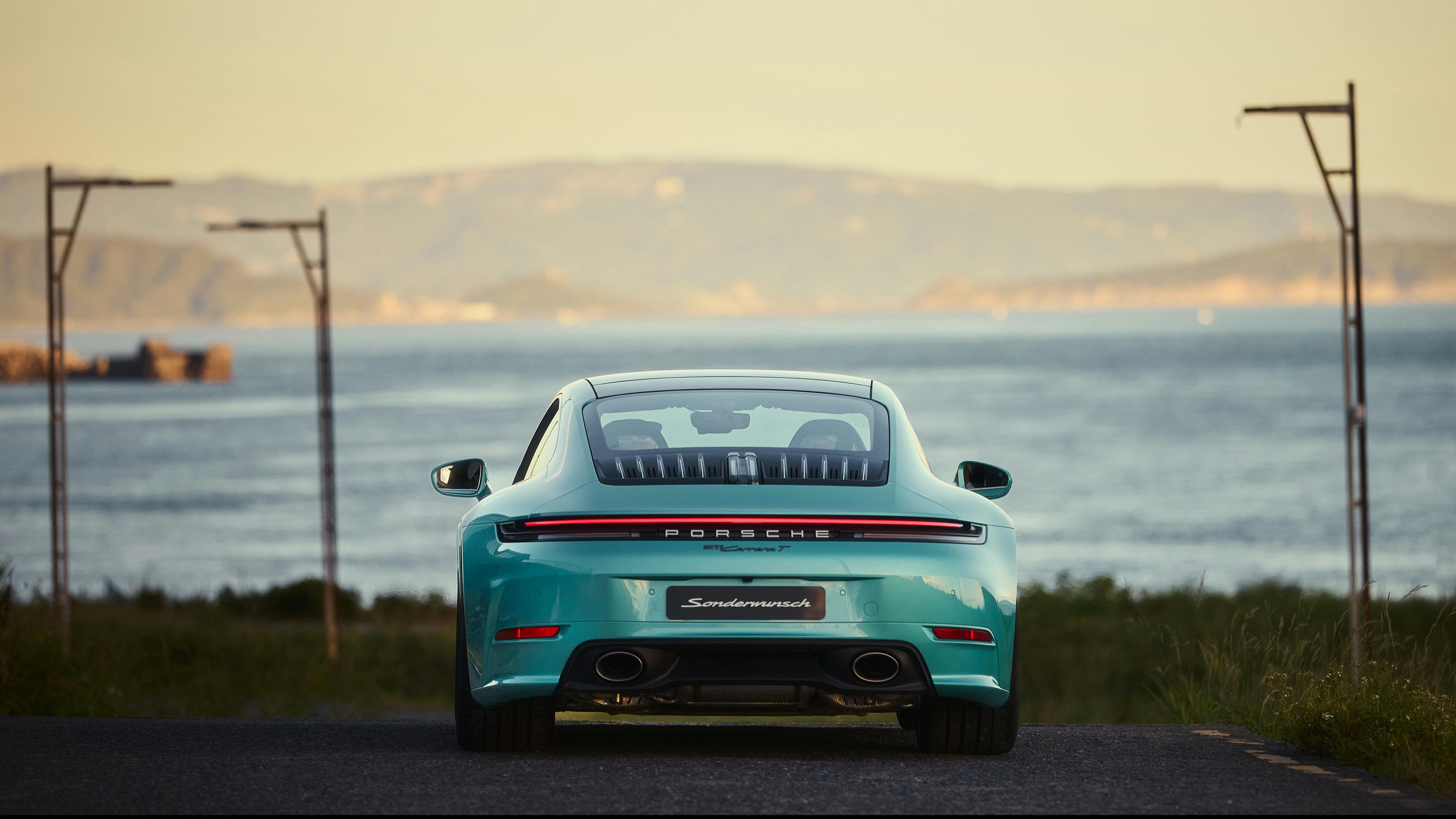 A turquoise Porsche 911 Carrera T parked on a mountain road, rear view with taillight strip, sea and island in distance.