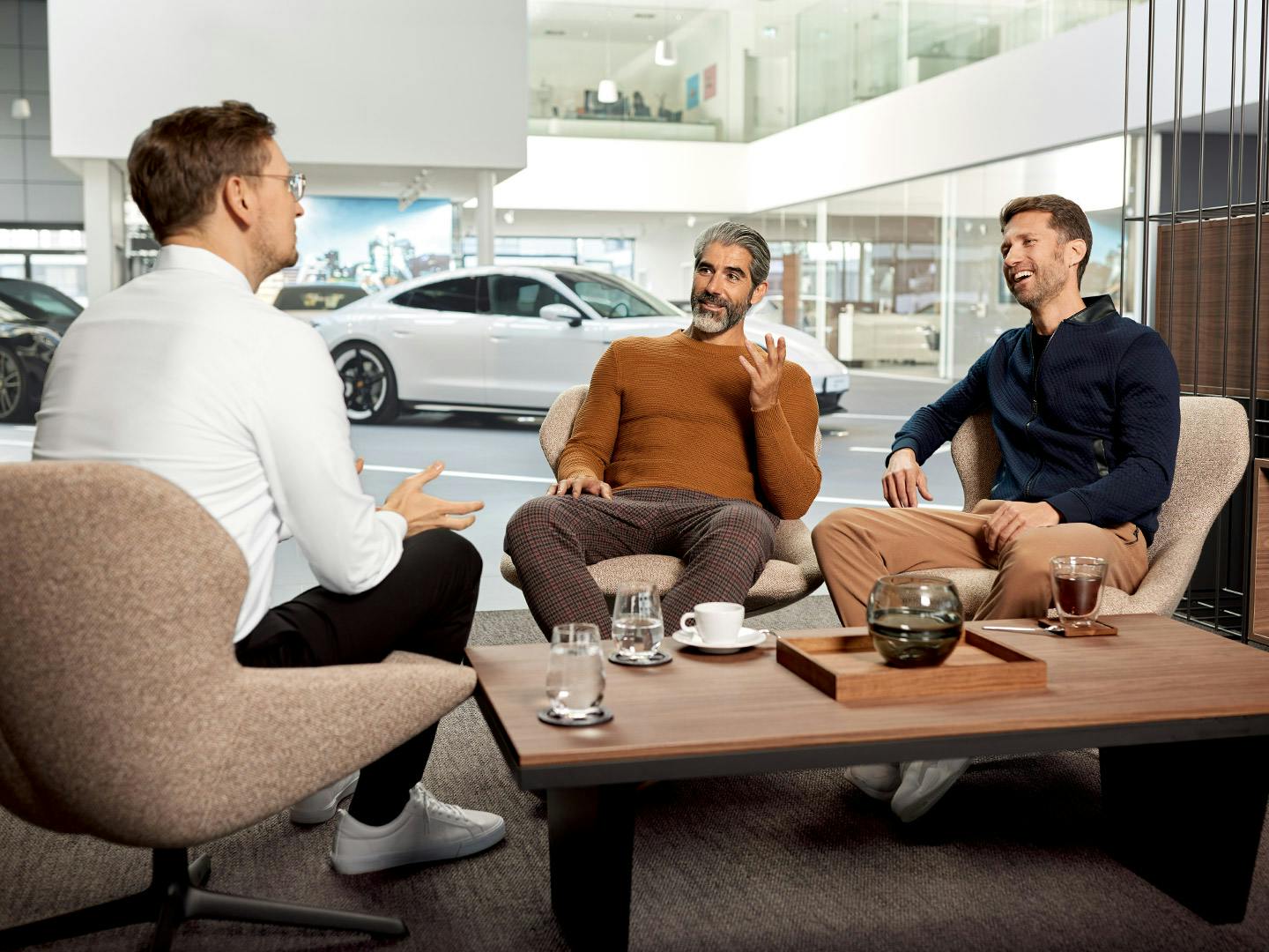 Zwei Kunden sitzen mit einem Porsche Kundenberater zusammen in einer Beratung im Porsche-Autohaus.