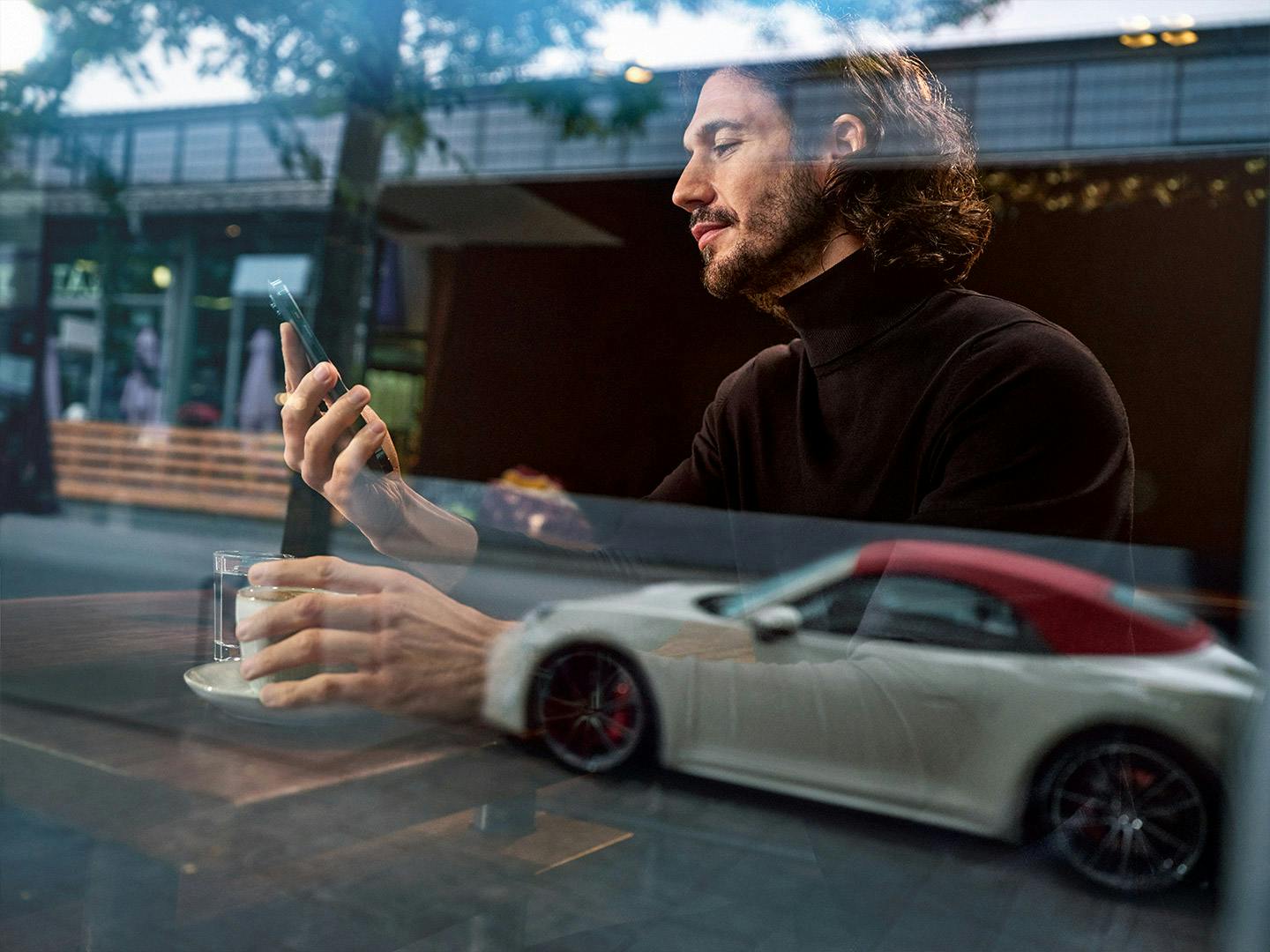 Un homme est assis derrière une fenêtre et regarde son smartphone.