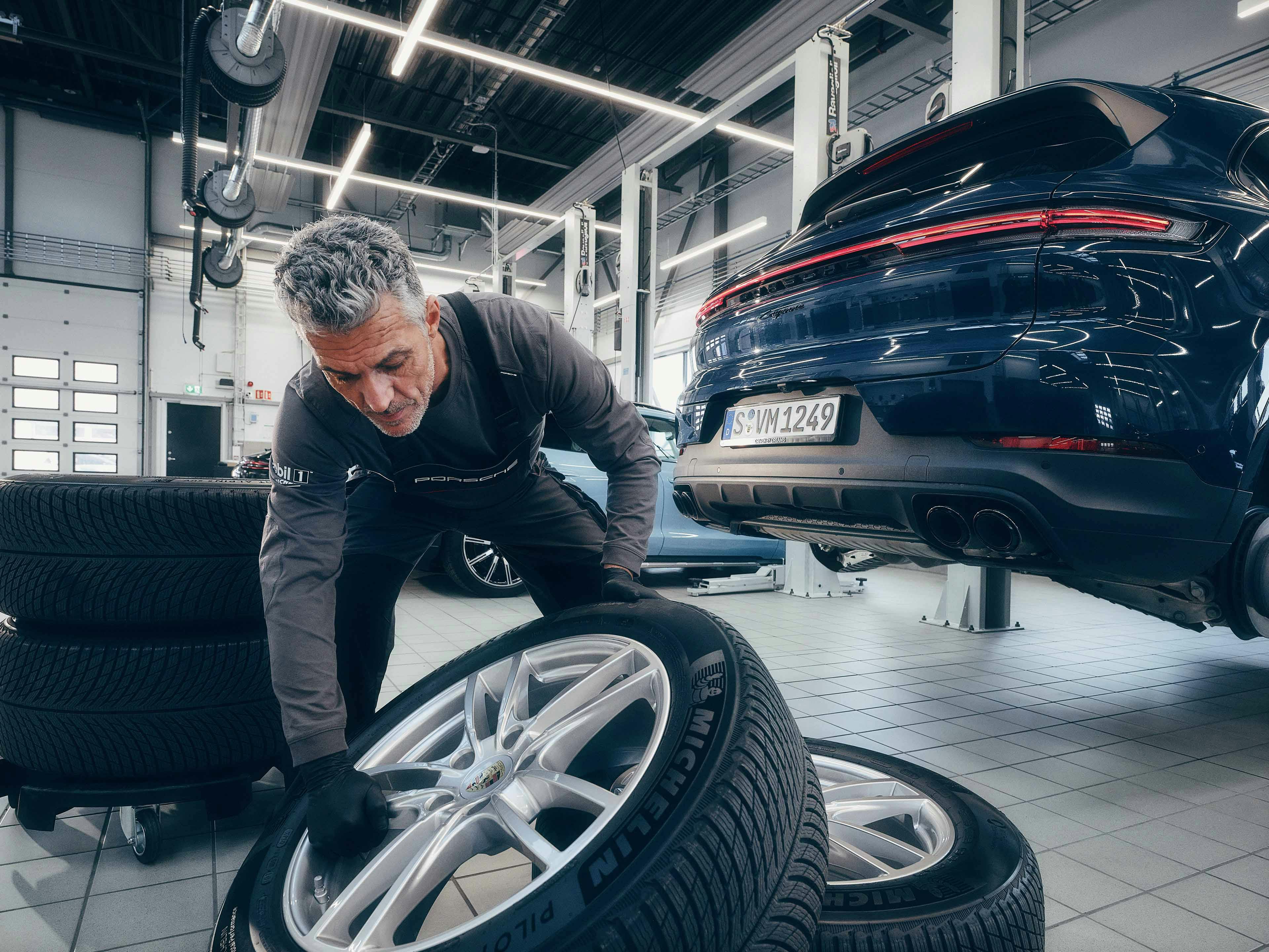 Een Porsche monteur houdt een nieuwe band vast voor een Porsche Cayenne.
