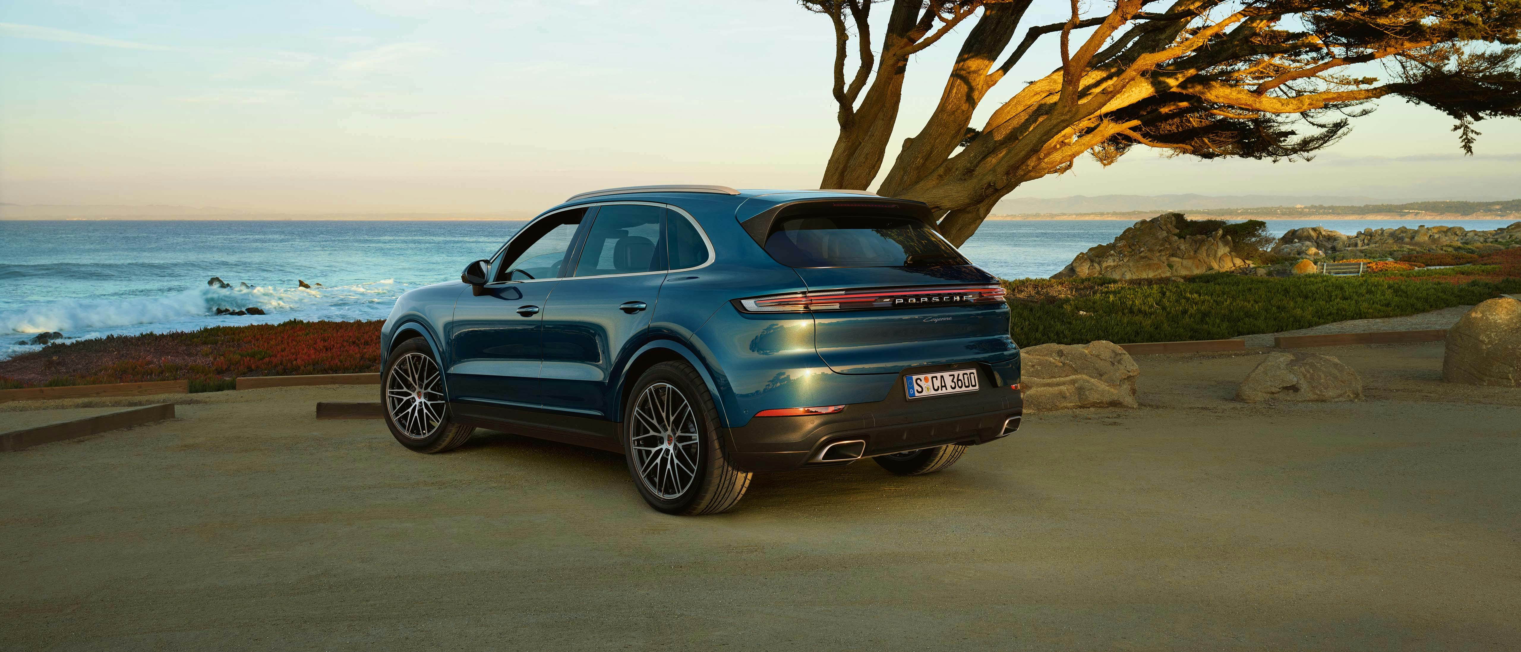Een blauwe Porsche Cayenne staat geparkeerd aan zee.